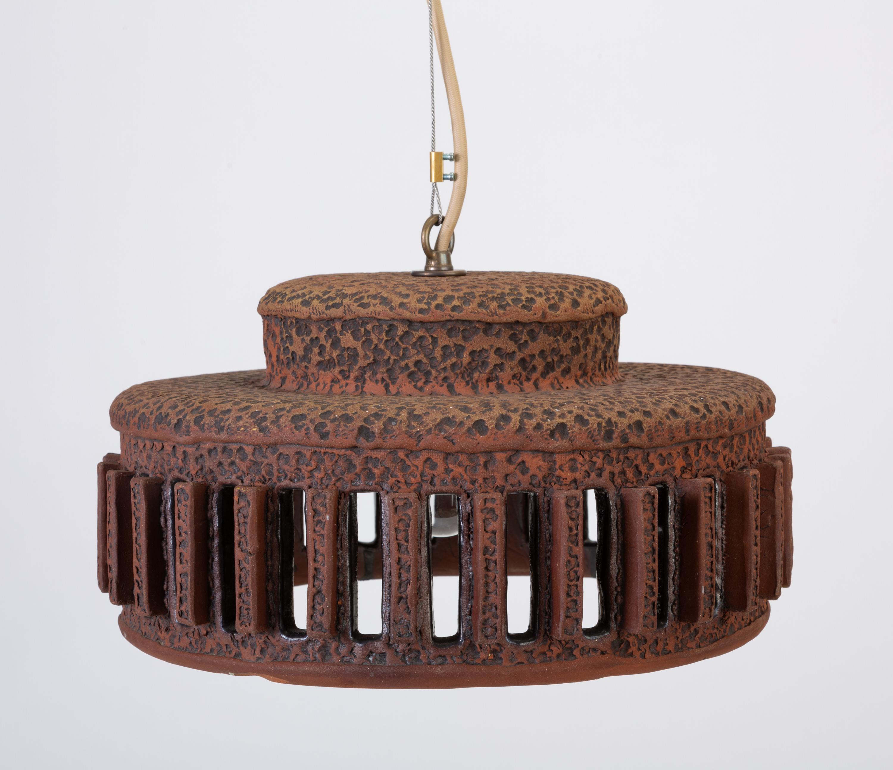 A unique stoneware pendant lamp with architectural, crenellated vents around the side. The lamp is made from a textured red-brown clay with handmade debossed and sgraffito detailing. This example has a low, wide drum shape with raised vents. The