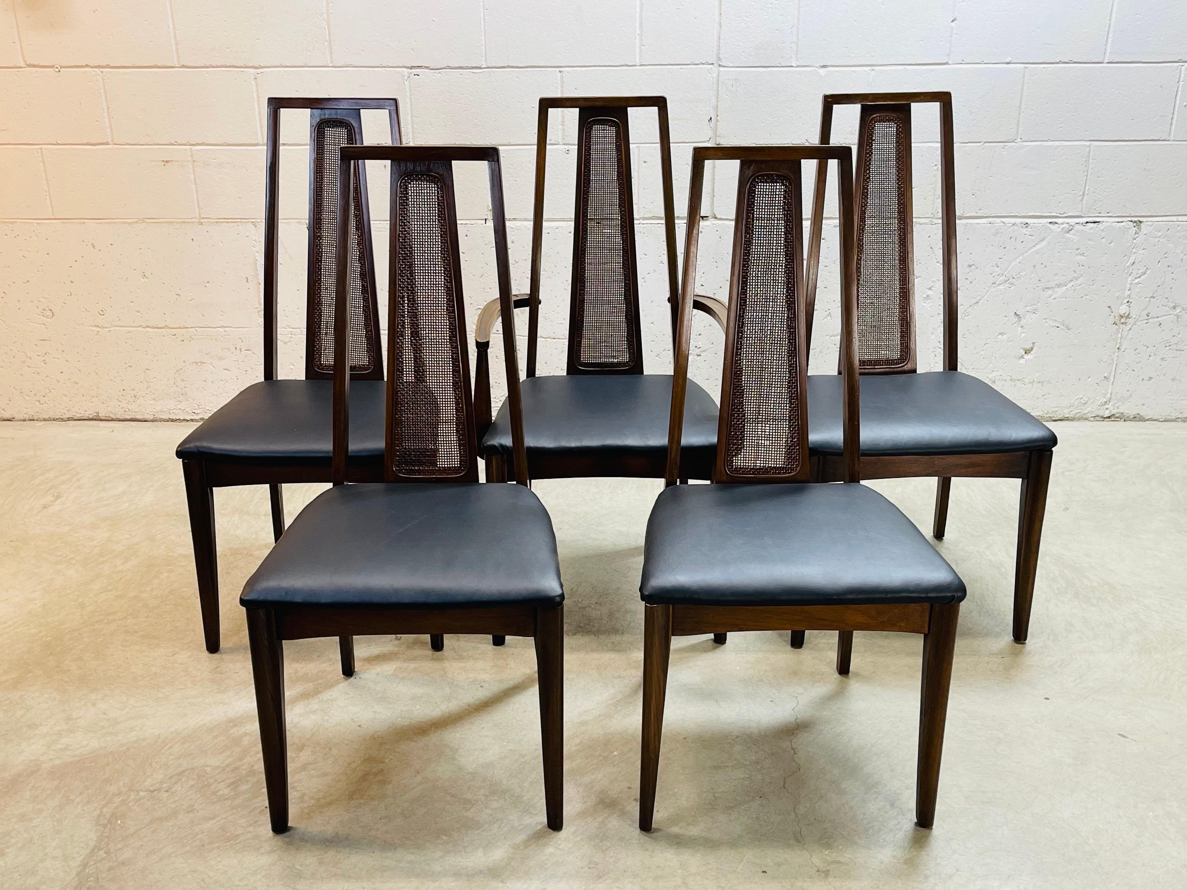 Vintage 1960s cane backed set of five dining room chairs. The set comes with a single captains chair. Arms 25.25”H. New black naugahyde seats. And all the chairs have been refinished. They are all strong and sturdy. No marks.