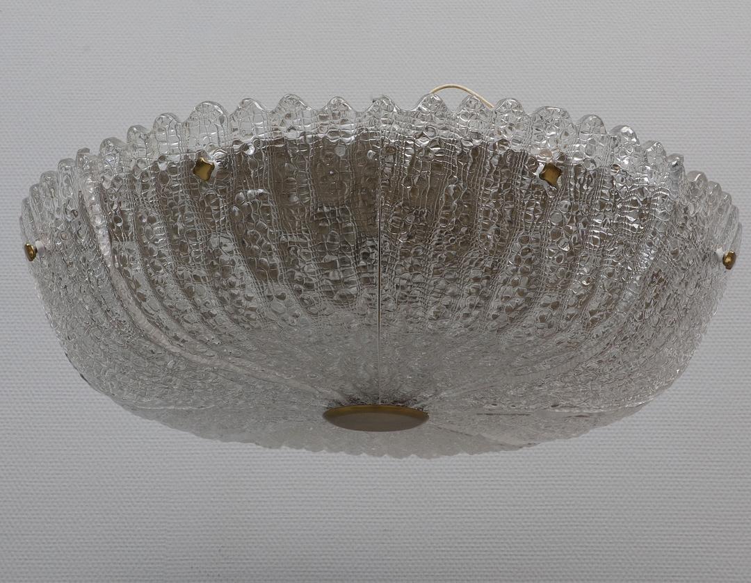 A Swedish Orrefors pendant designed by Carl Fagerlund (1915-2011) in its original aged brass finish; the thick clear blown and cold-worked glass having a stippled and gullied surface with a saw-toothed edge concealing eight electric candelabra