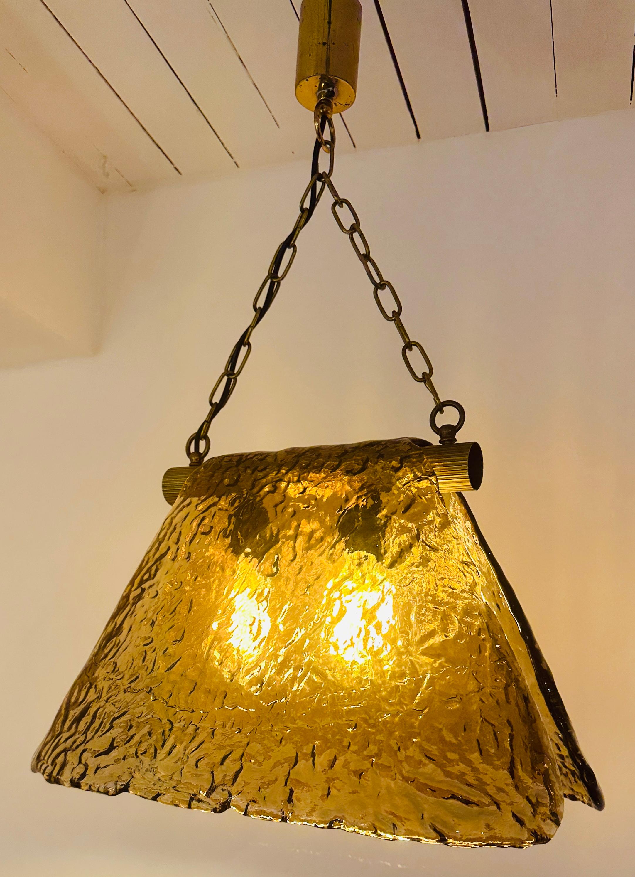 A stunning 1960s Italian Murano glass and brass hanging ceiling light designed by Carlo Nason for Mazzega.  A single piece of heavy and thick Murano glass is folded over a polished brass horizontal cylinder and suspended from a matching brass chain.