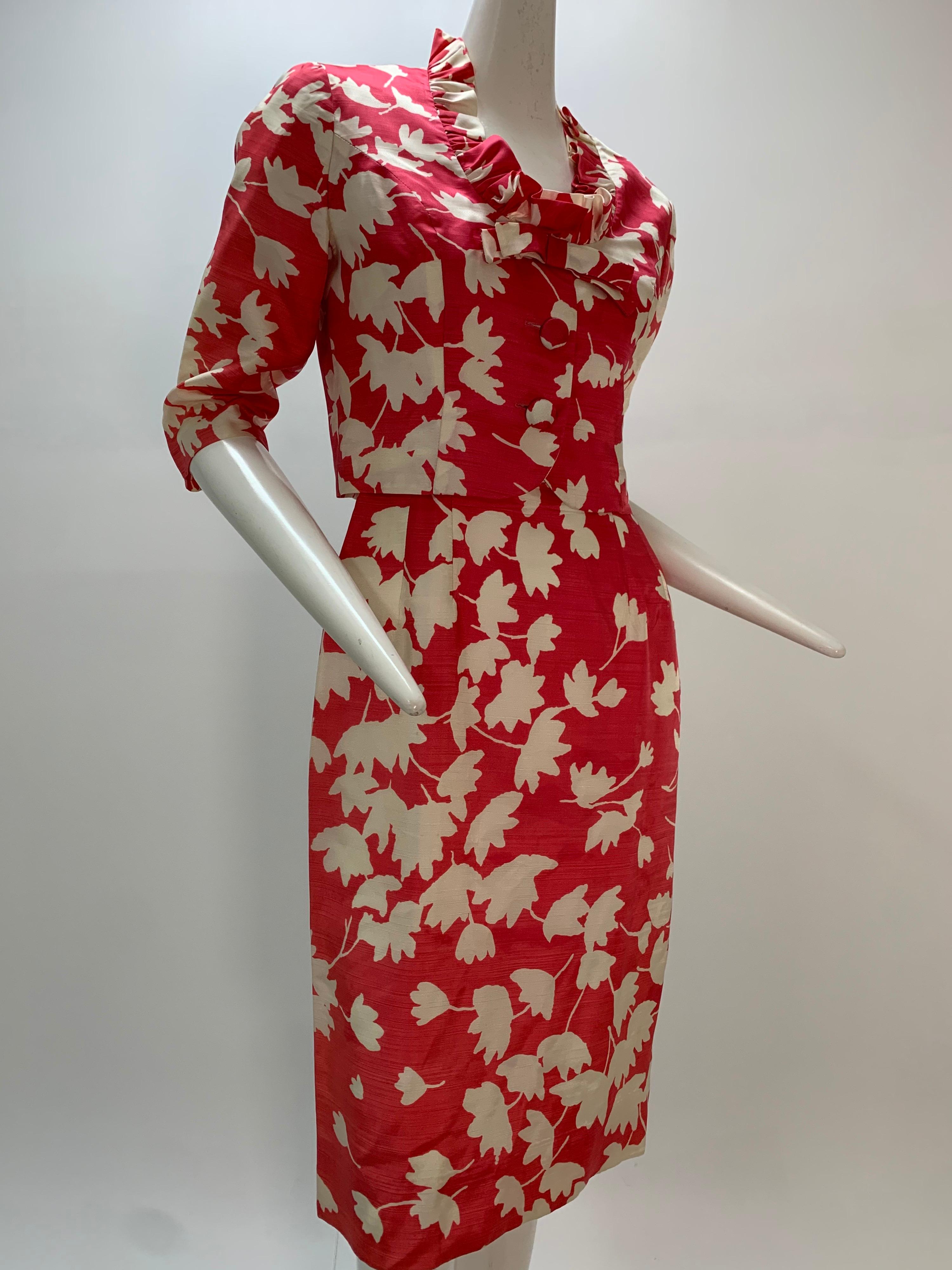 A striking 1960s Carol Craig dress and cropped jacket ensemble: Beautiful white floral silhouettes on a shocking pink ground cover this short-sleeved, ballerina-neckline fitted dress and ruffled-collar cropped jacket. Buttons down front of jacket.