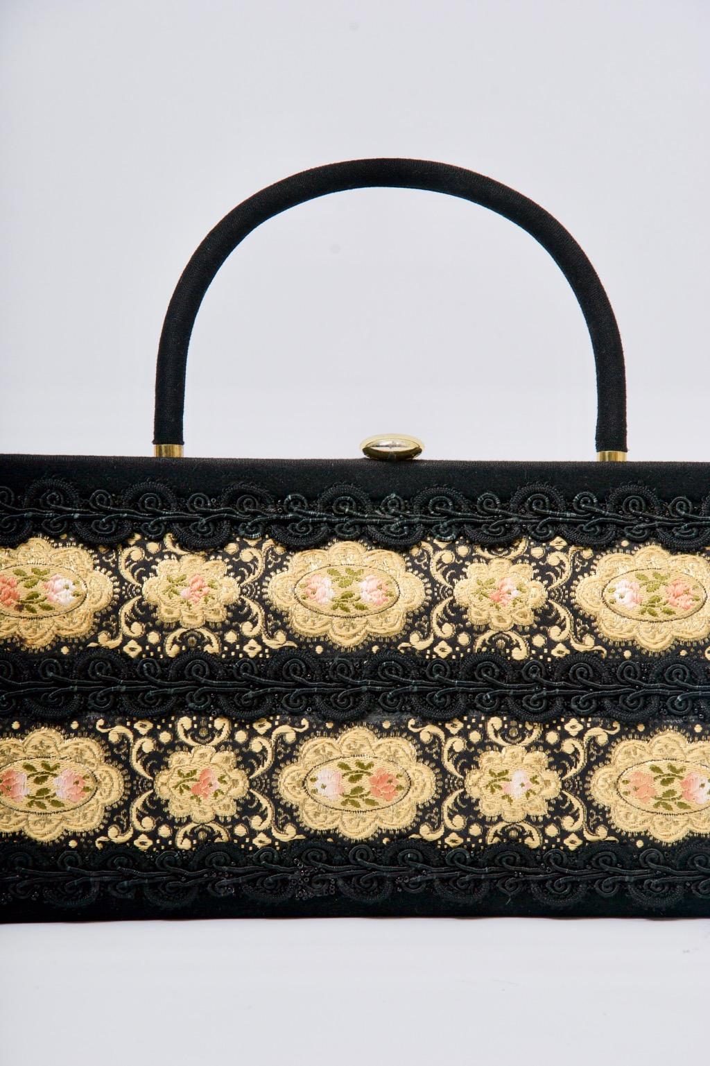 1960s elongated handbag of soft black fabric embellished on front with a double row of ribbon trim bound edged with black soutache. Single structured handle and gold disk clasp. Caron of Houston was known for its hand decorated handbags, very