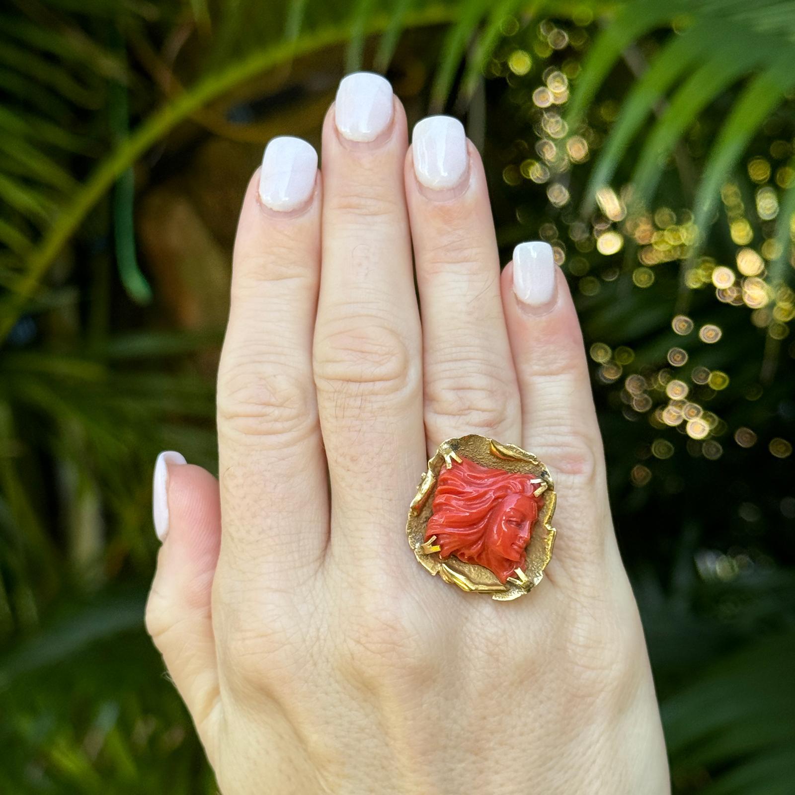 Carved coral estate ring handcrafted in 18 karat yellow gold. The ring features a carved solid orange coral set in free form 18 karat yellow gold. The ring is currently size 7 (can be sized) and the top measures 1.25 x 1.25 inches. The shank