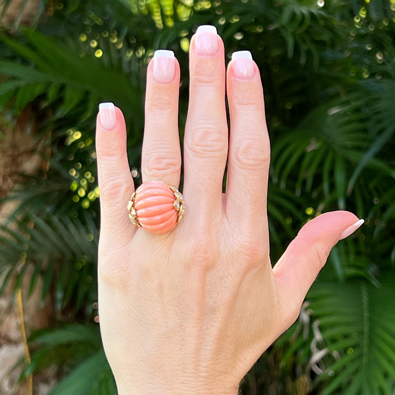 Beautiful carved coral and diamond dome cocktail ring handcrafted in 18 karat yellow gold. The ring features a coloful orange carved ribbed coral gemstone set with 12 round brilliant cut diamond accents. The diamonds weigh approximately 1.00 CTW and