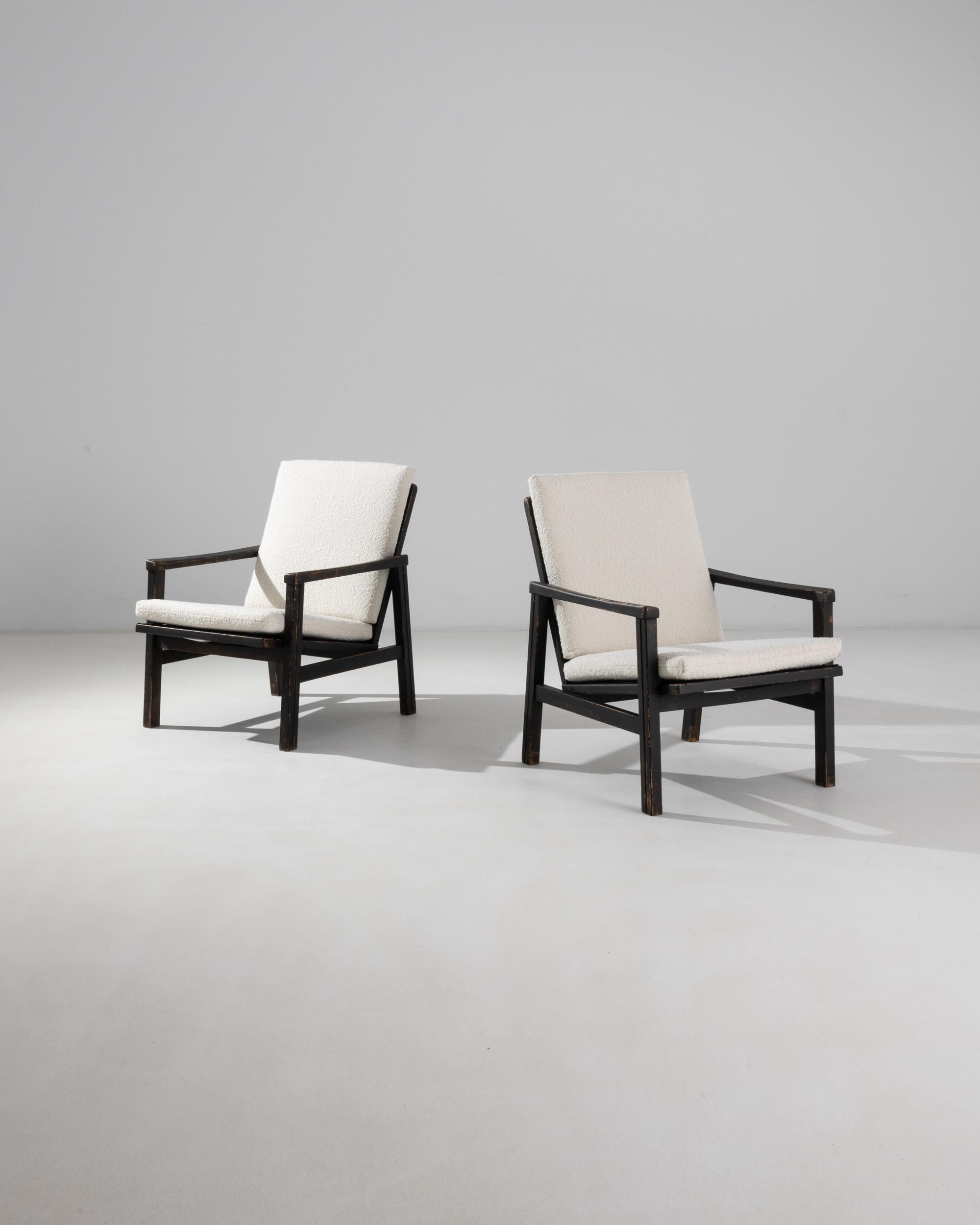 These upholstered armchairs were produced in Czechia, circa 1960. Upholstered with a fluffy white boucle, the slight recline and cushioned seat make for a comfortable posture. Contrasting with the angular dark coffee frame and wooden slats of the