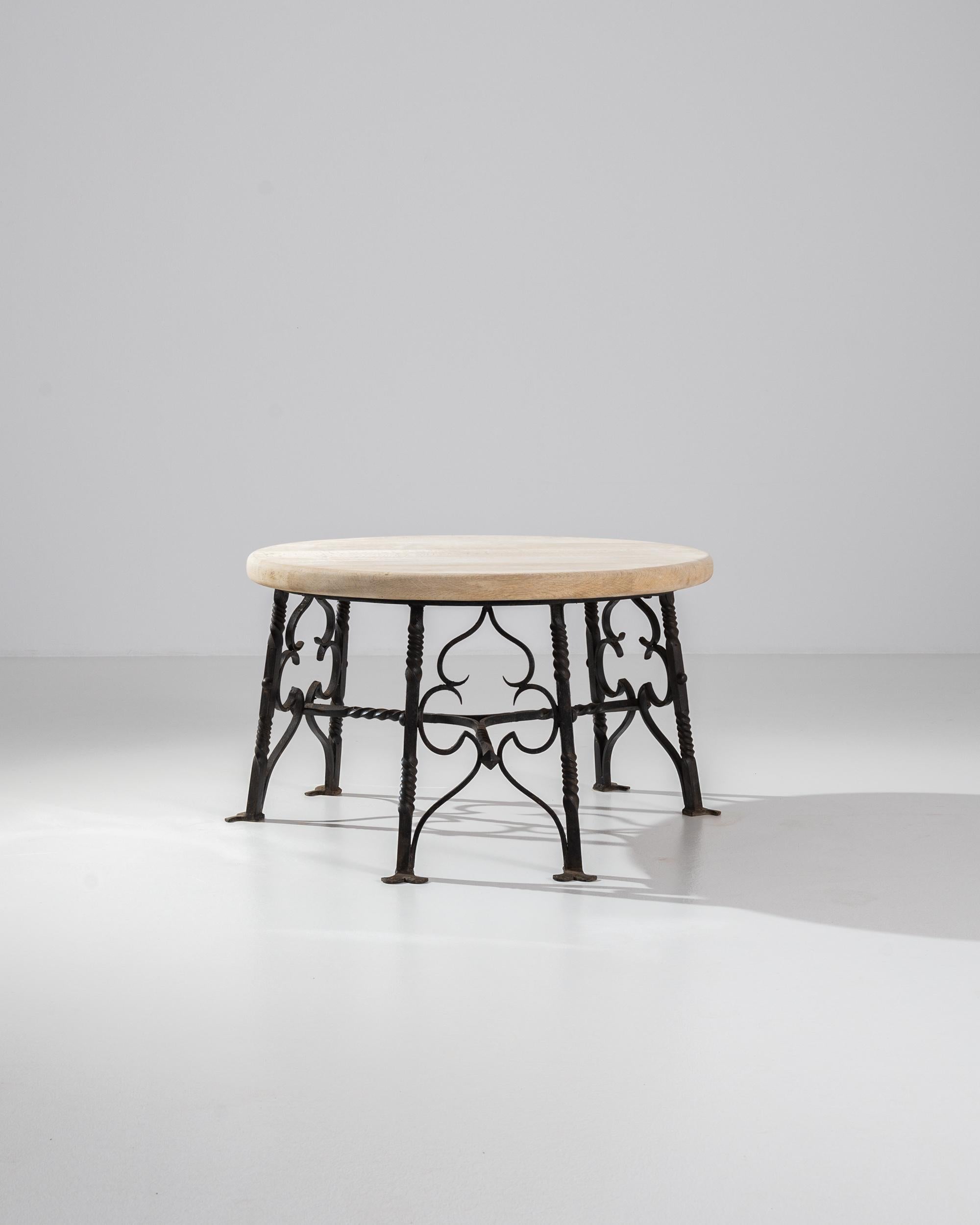 Elegant and striking, this 20th century coffee table combines contemporary forms with gothic elements for an eclectic composition. Sourced from France, a circular tabletop of pale wood sits atop a frame of wrought iron tracery. The skillful