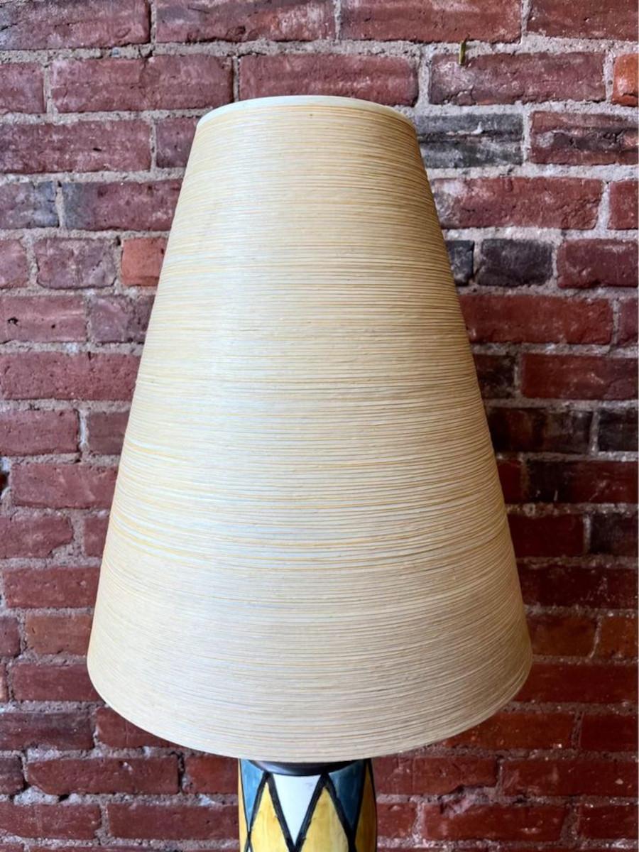 We are thrilled to offer this exquisite 1960s Handpainted Ceramic Table Lamp by Lotte and Gunnar Bustland. Adorned with an original fiberglass shade meticulously handpainted by the artists themselves, featuring a harmonious crisscross pattern in