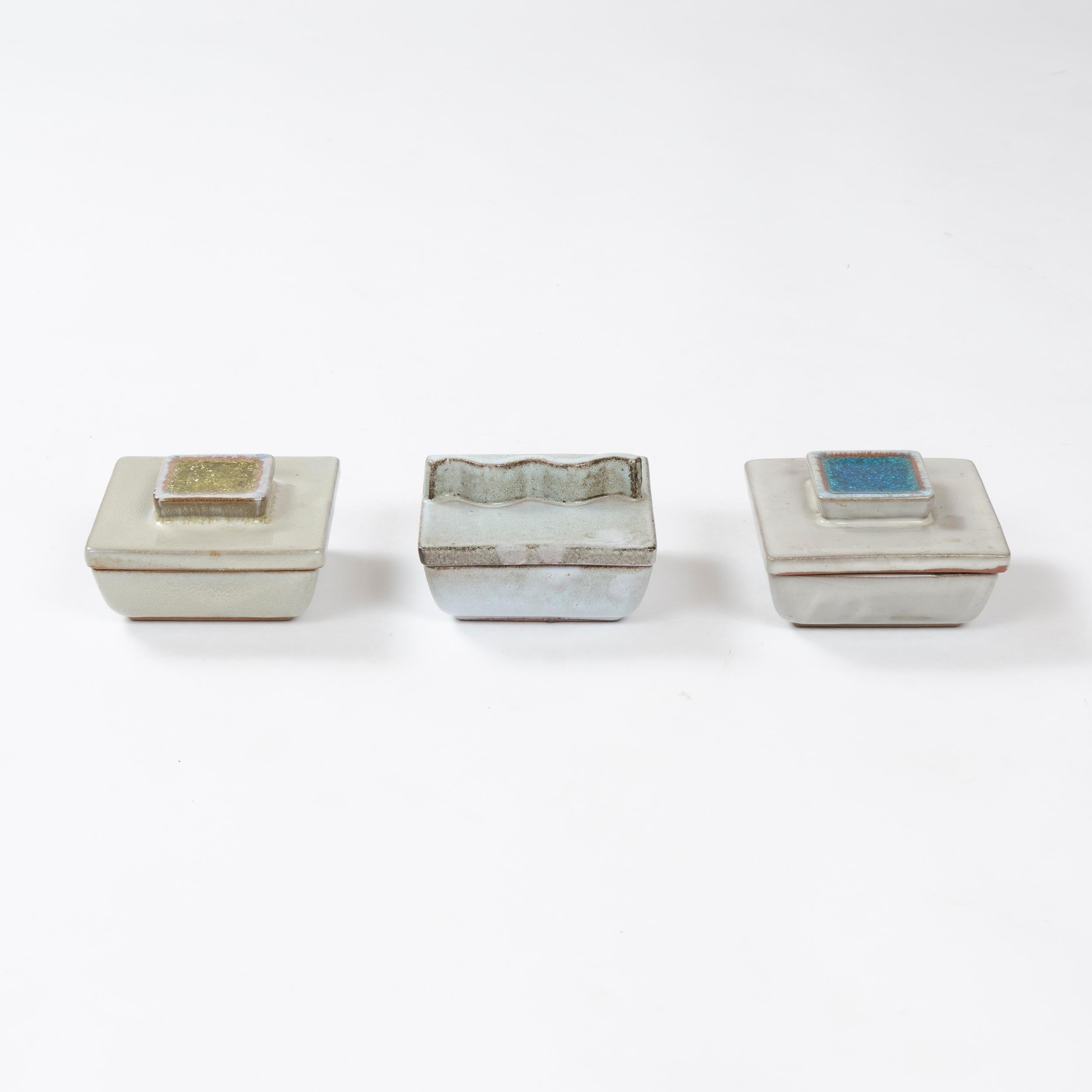 A set of three ceramic lidded boxes, two with crackled glass inlaid handles and one with a squiggle cut handle.