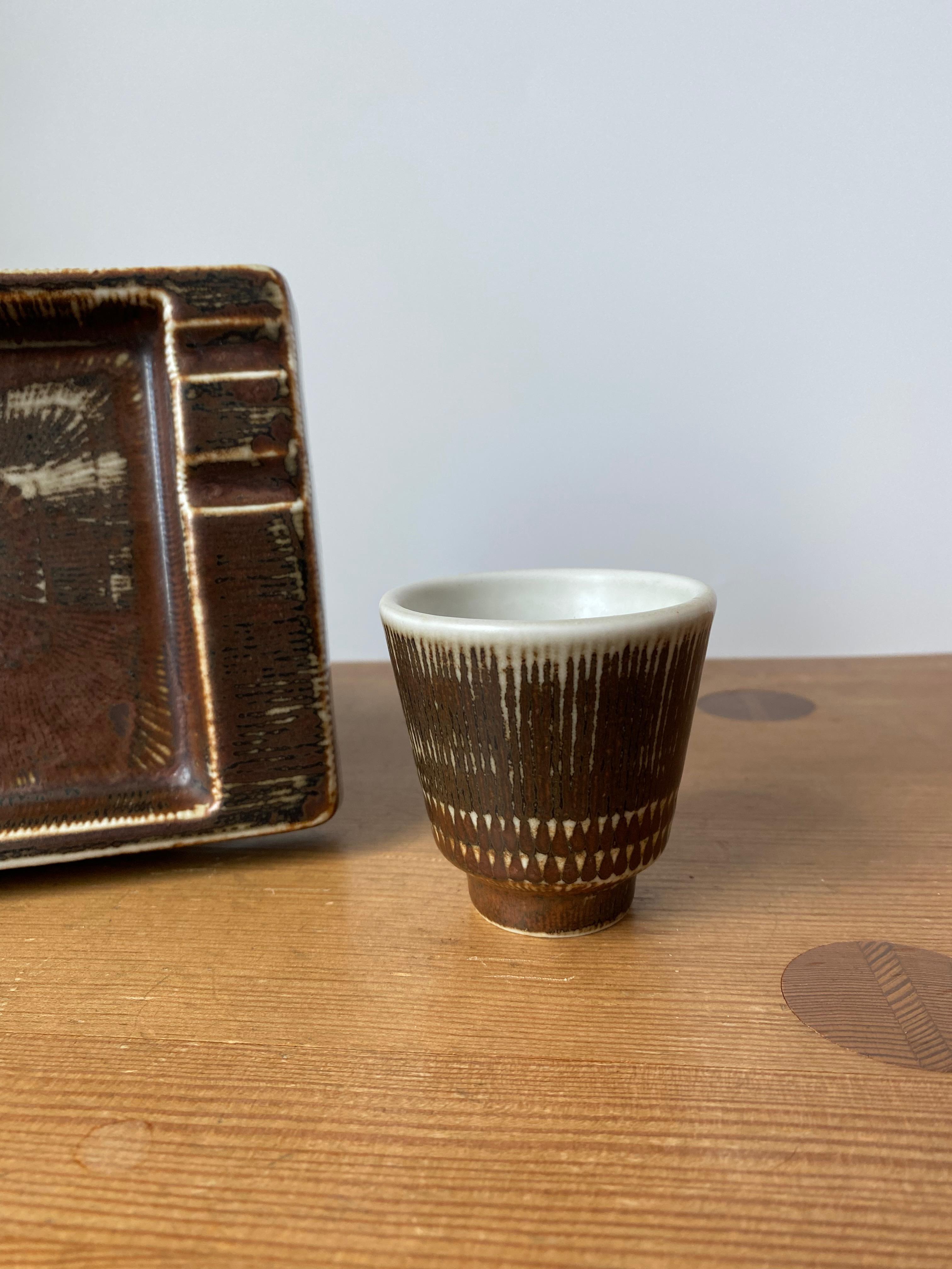 Set in ceramica del 1960 di Hertha Bengtsson per Rörstrand, Svezia. Si tratta di un piatto rettangolare e di un vaso in miniatura con uno splendido smalto marrone con dettagli a strisce bianche. Marcato in basso con la firma del designer e in ottime