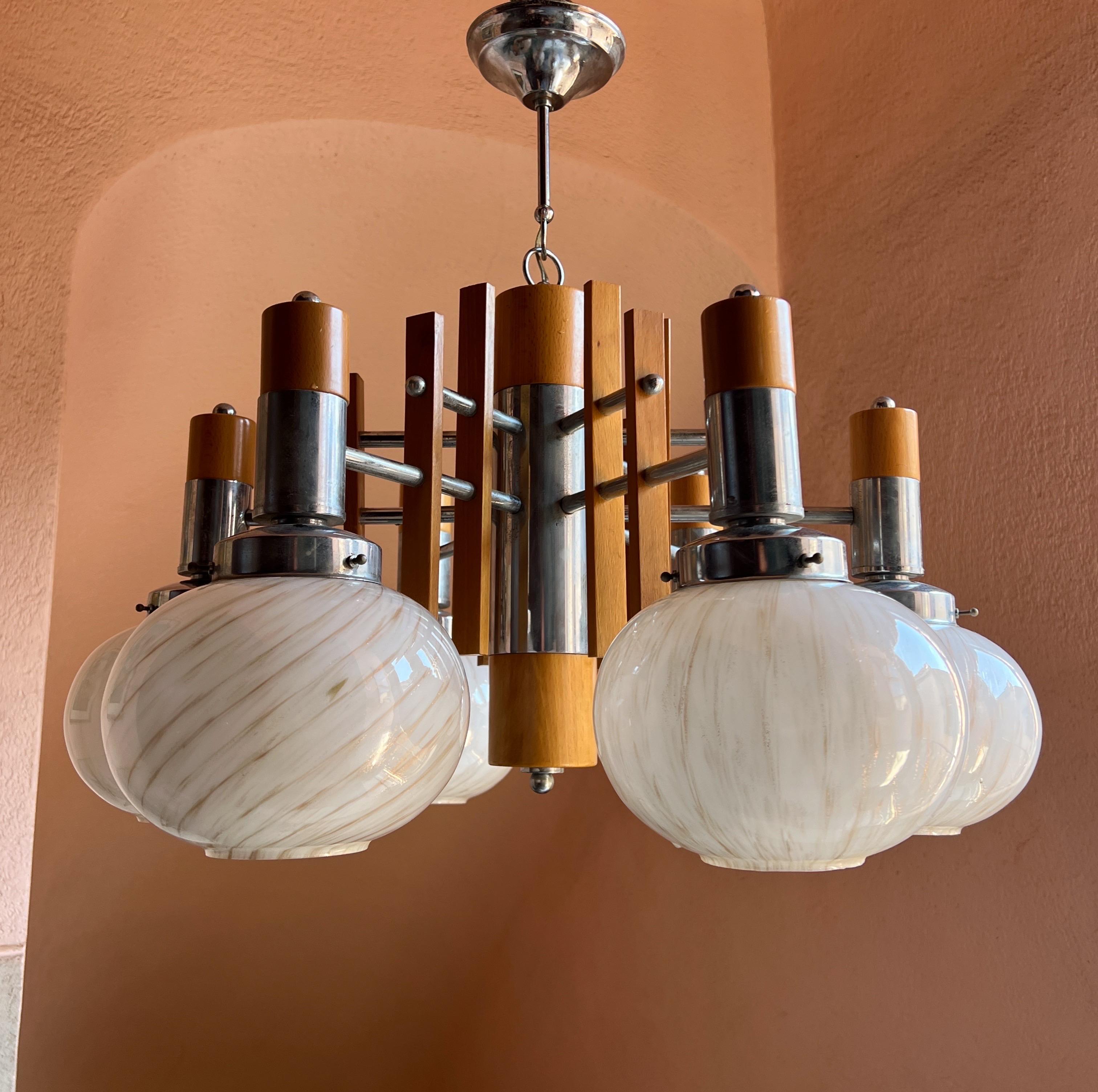Stunning mid-century modern chandelier by Mazzega, Murano, circa 1960. This elegant fixture features six Murano glass spheres attached to a base combining sleek chrome and warm wood, offering a Scandinavian-inspired design.

The Murano glass spheres