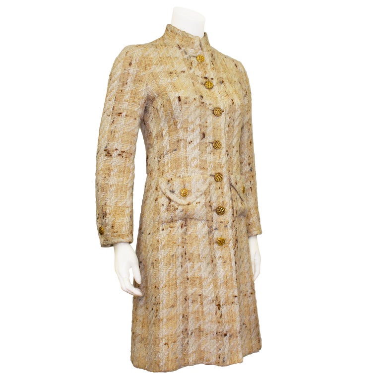 An incredible Chanel Haute Couture coat from the 1960s. This piece is made from lightweight beige and white woven wool tweed and is embellished with warm gold tone metal round buttons with a woven motif. The jacket features a standing collar and two