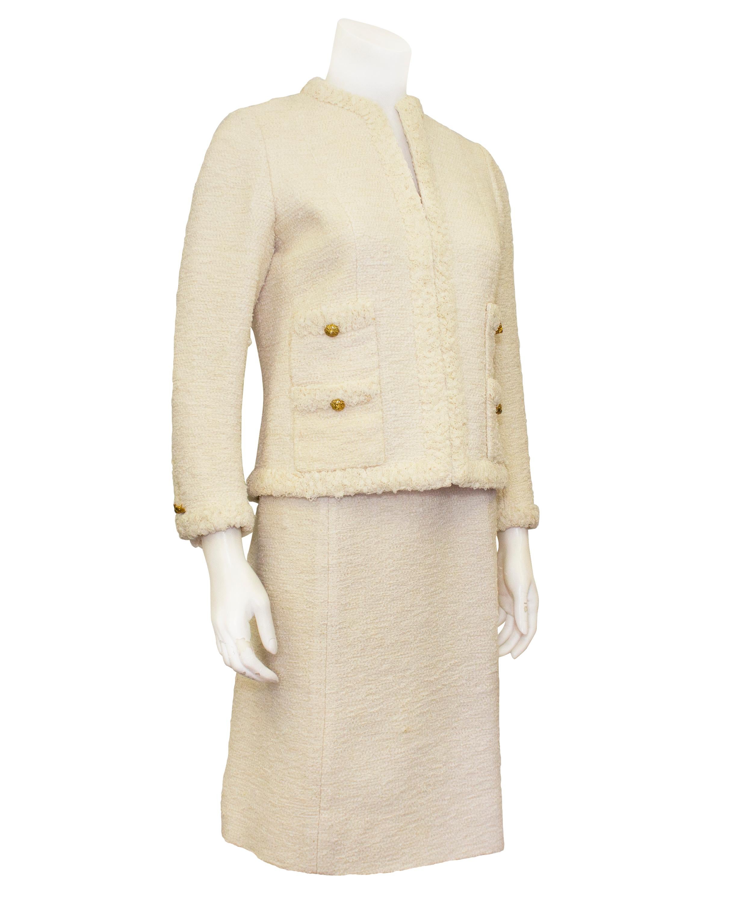 A subtle and effortlessly stunning cream tweed Chanel Haute Couture skirt suit from the 1960s. The jacket is collarless with four patch slit pockets and hook and eye closures. The jacket is fully trimmed in ruched lace that creates a fringe like