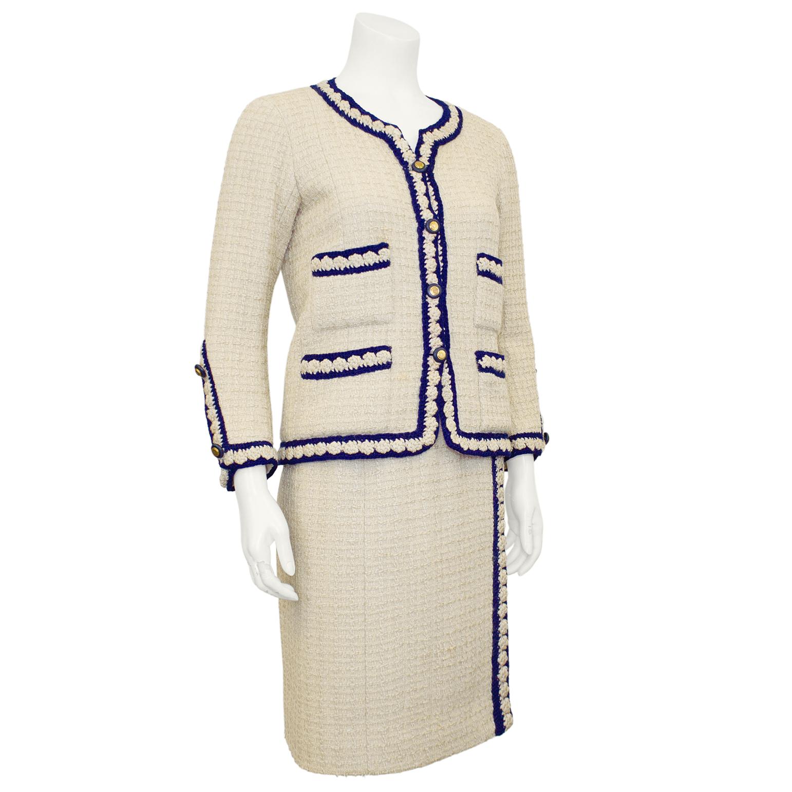 Combinaison emblématique de Chanel Haute Couture des années 1960, composée d'une boucle de laine crème et d'une bordure tressée marine, fermée par des boutons en métal doré sertis de bleu marine. Ce tailleur représente le look classique et