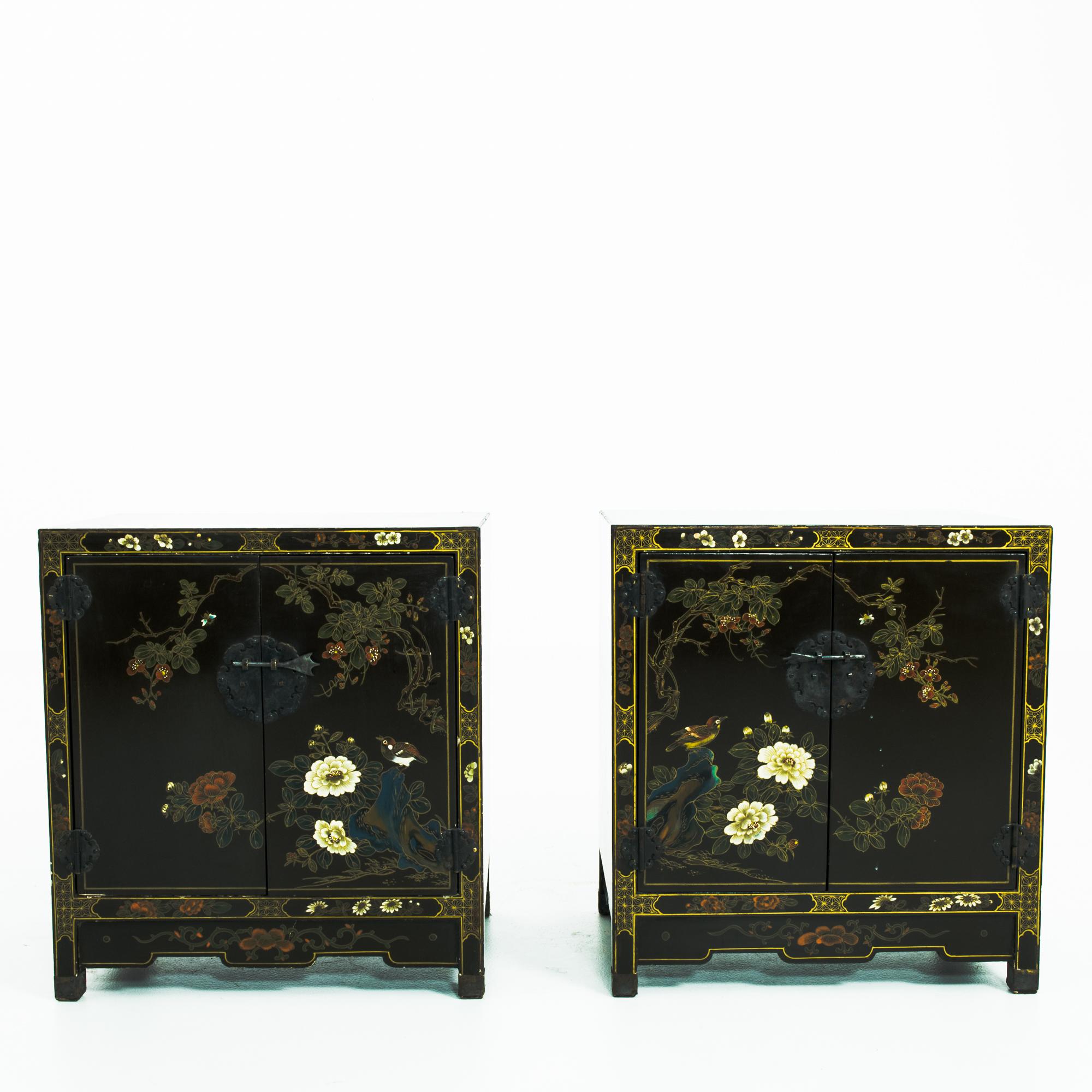 A pair of wooden bedside tables from China, circa 1960. Lacquered wood is decorated with an intricate design of chrysanthemums, plum blossoms and nightingales; gold geometric motifs mark the borders of the frame. The rich colors and exquisite detail