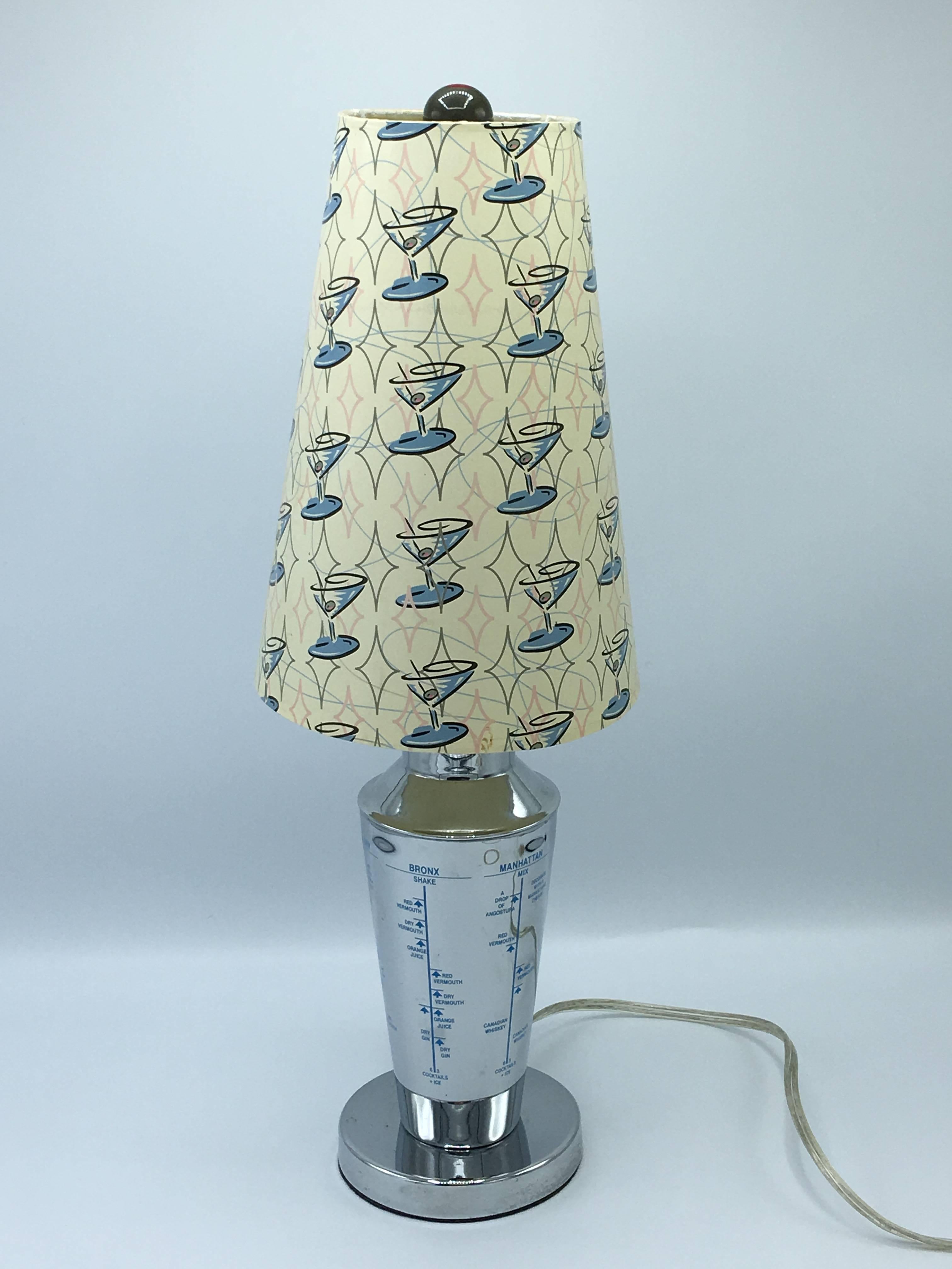 Offered is a fabulous and quirky, 1960s chrome martini Shaker lamp with a coordinating shade and finial. The shade has a retro martini print on it, with a matching olive finial. Rewired.