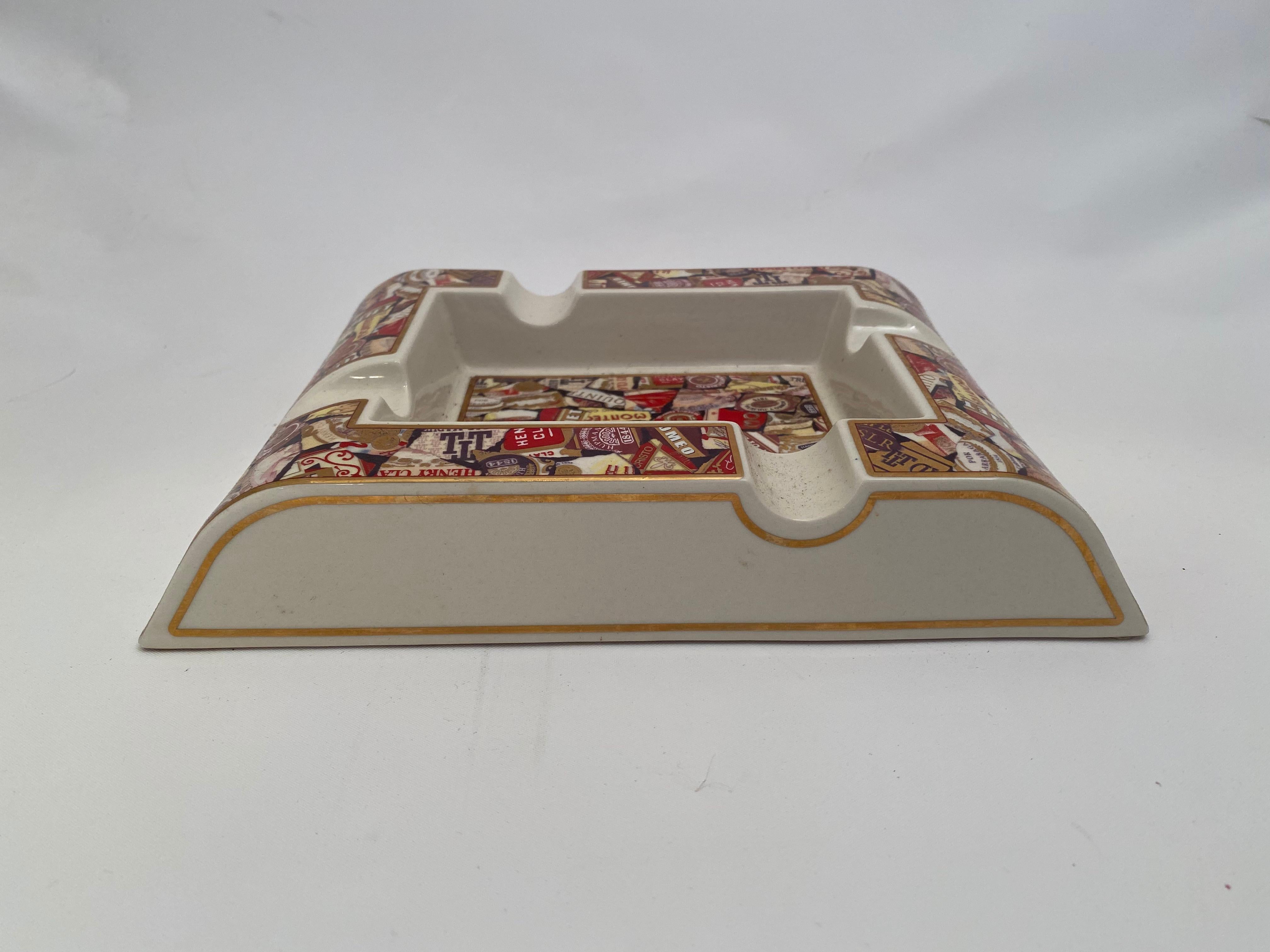 Large and commodious screen printed cigar band cigar ashtray. Gold leaf banding detail with a wonderful collage of numerous famous cigar brand bands. 

Very good condition with no visible chips, cracks, hairlines, stains or restorations. Porcelain