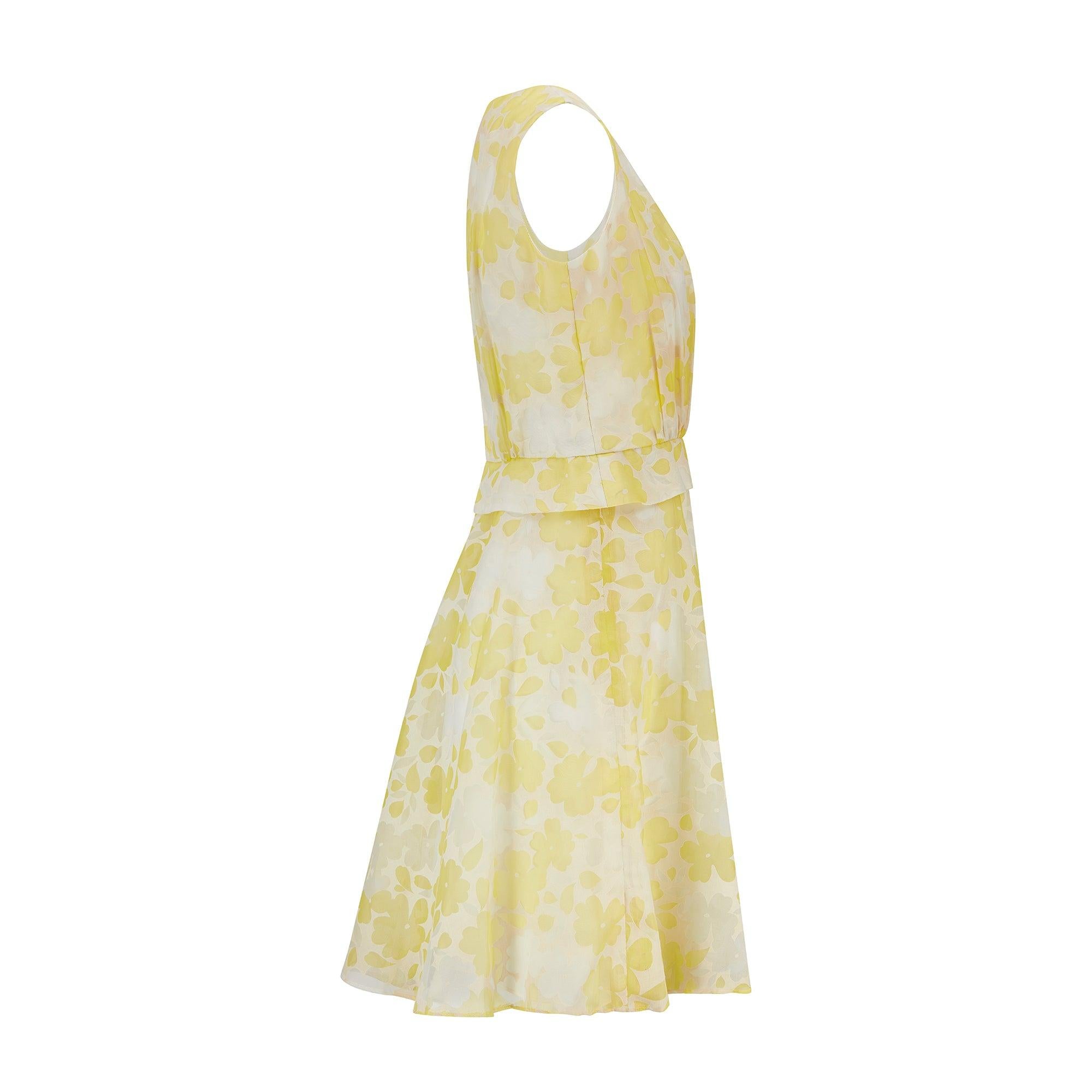 This pretty dress was designed by Claire Layton in London during the 1960s. It is tailored from manmade white medium weight chiffon woven with sheer flowers in yellow and white. These florals really pop against the white satin lining. Cut to a