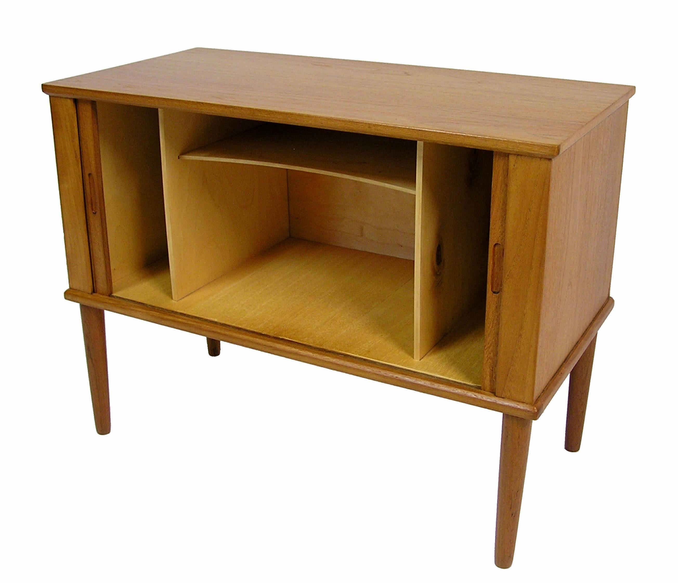 A small teak record cabinet from the 1960s Danish modern era. Similar in design to those by Kai Kristiansen this unique tambour door storage cabinet features a low compact form with tapered conical legs and inset modern era pulls. Inside of the