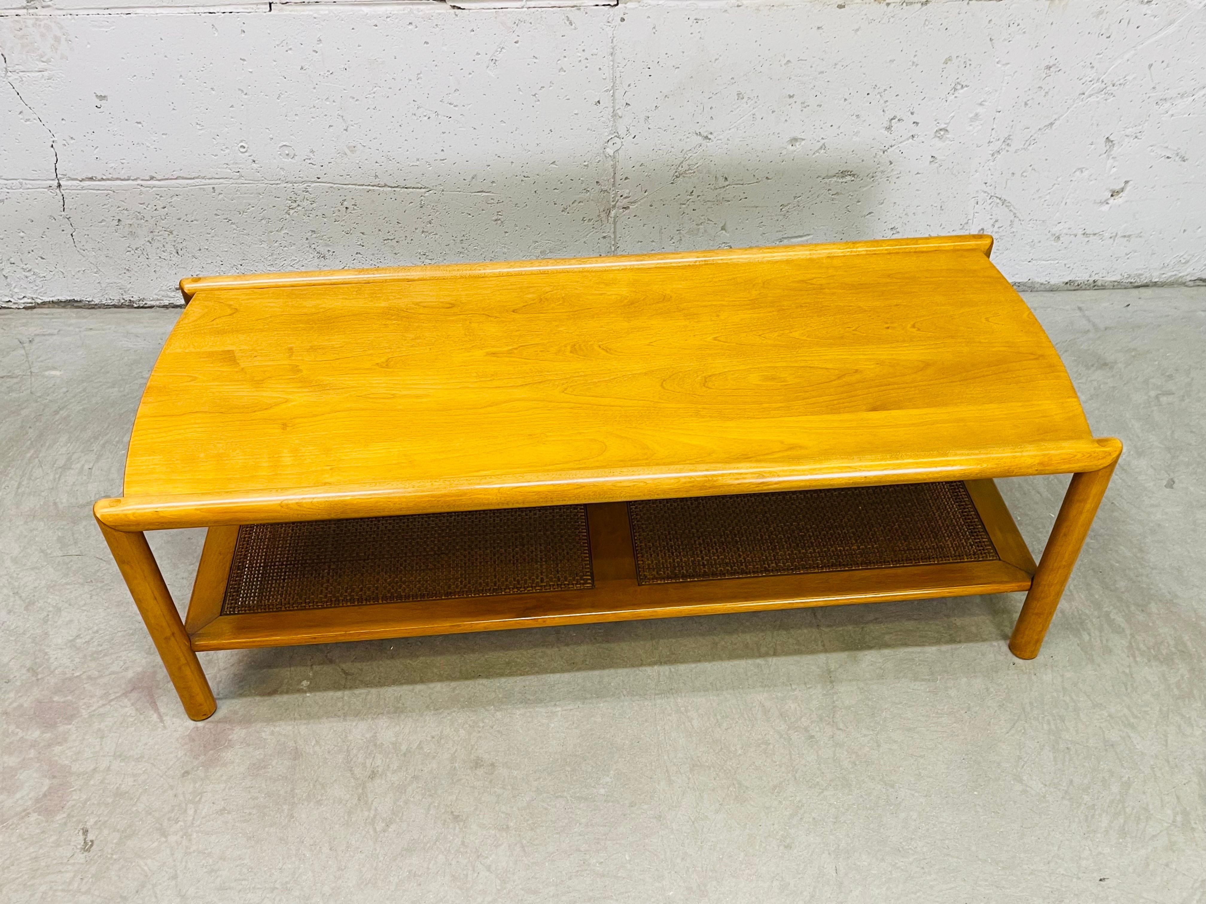Vintage 1960s Conant Ball maple wood rectangular coffee table with wicker shelf. The shelf has two wicker panels for additional storage. Wicker is in excellent condition. Top of the table shows the peg style joinery. Excellent condition. Marked