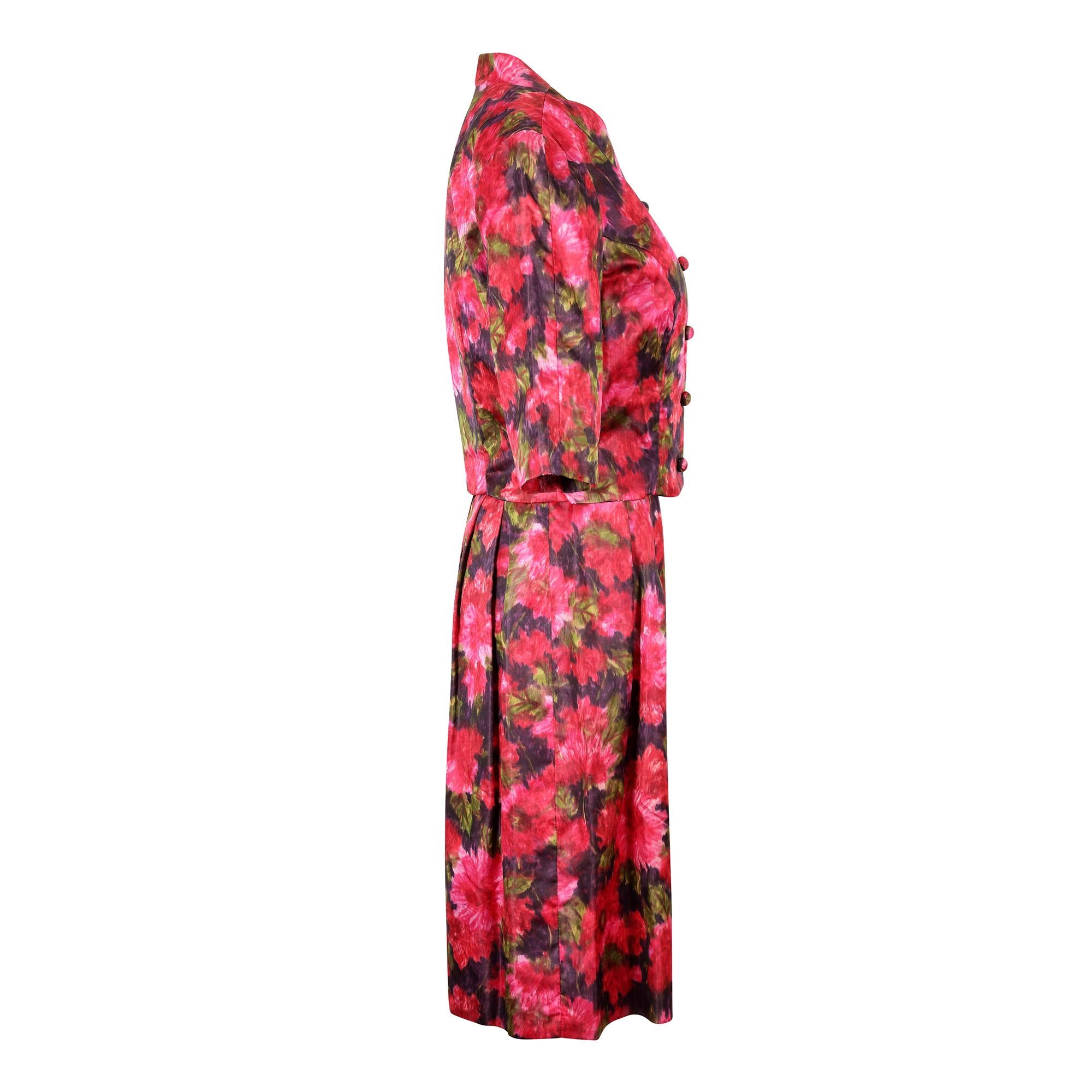 This early 1960s silk satin floral printed dress suit has an attractive floral print in bright shades of cerise pink, red and purple and reminiscent of an impressionist painting. There are some very good quality design details on the dress including