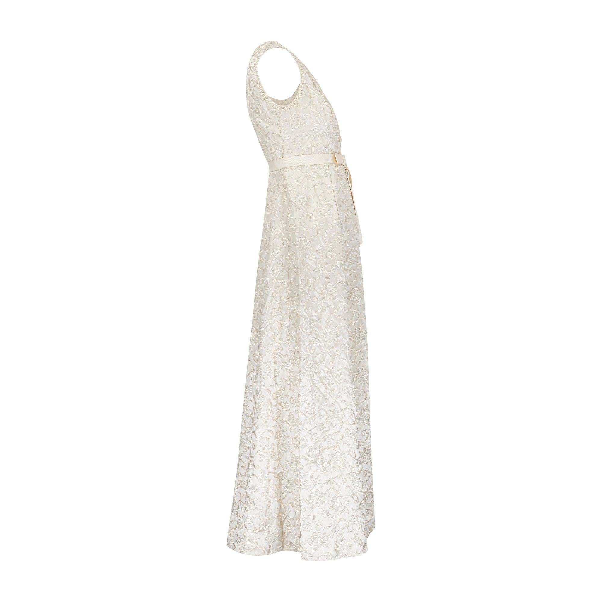 Este opulento vestido de los años 60 es un hallazgo raro. Con detalles inusualmente complejos, está confeccionado en satén brillante de color crema pálido y bordado por todas partes con enredaderas en espiral y un surtido de flores, incluidas rosas