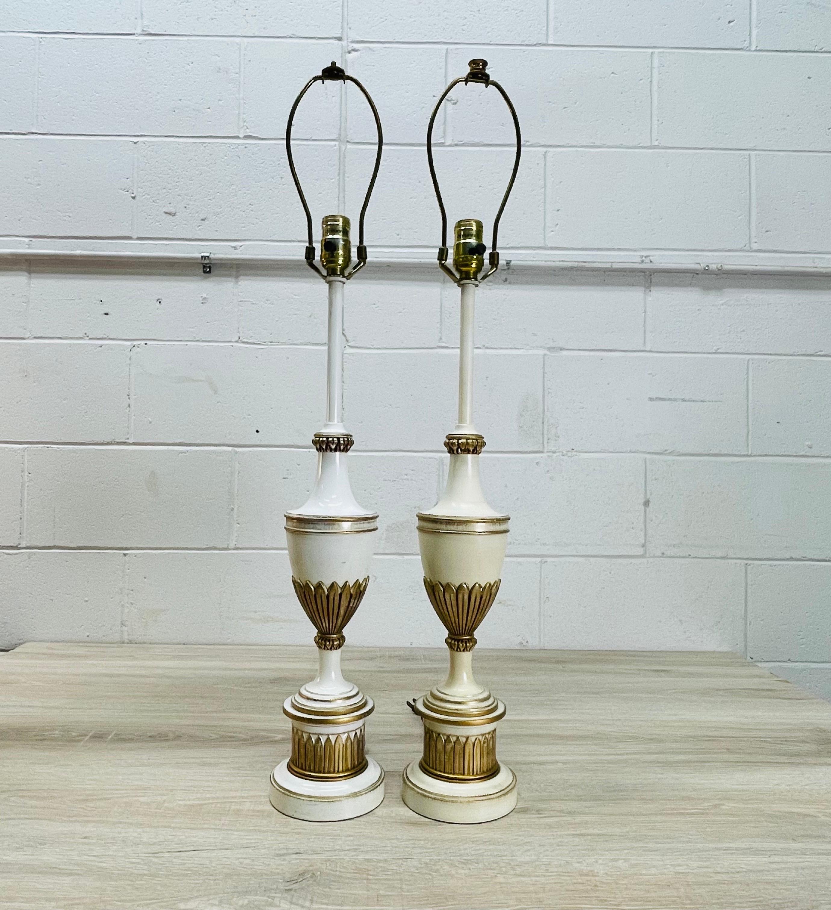Vintage pair of Stiffel cream and gold metal table lamps. The lamps have a gold leaf design. Wired for the US and in working condition. The lamps use a standard 100W bulb. Socket, 25”H. Harp, 4”Dia x 8”H. One finial is missing and one lamp is