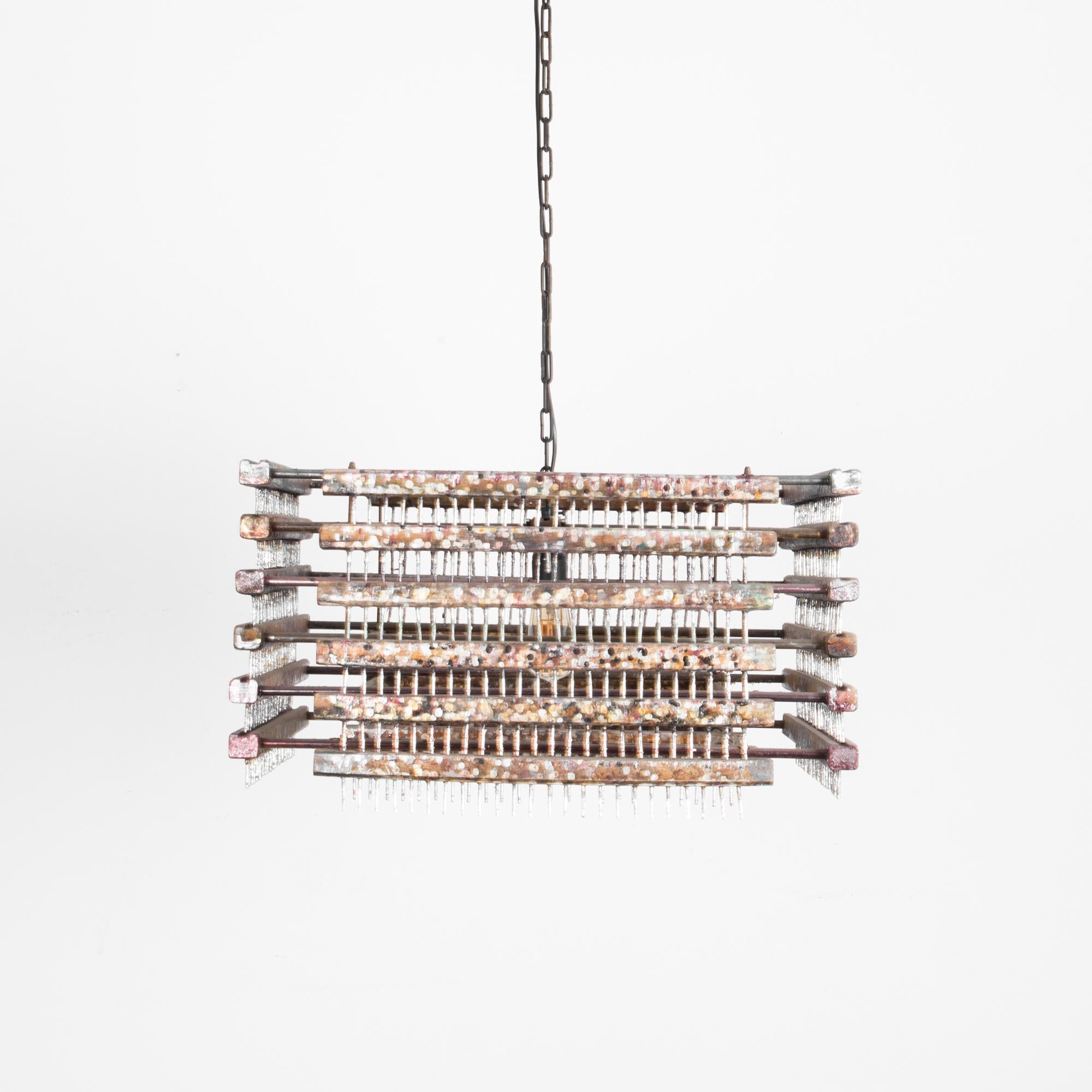 This metal pendant light was made in Czechia in the 1960s.  A ceiling chain sustains a square light fixture made of a grid of metal bars for a stark, brutalist silhouette. The industrial sensibility of the interlocking metal bars is softened by