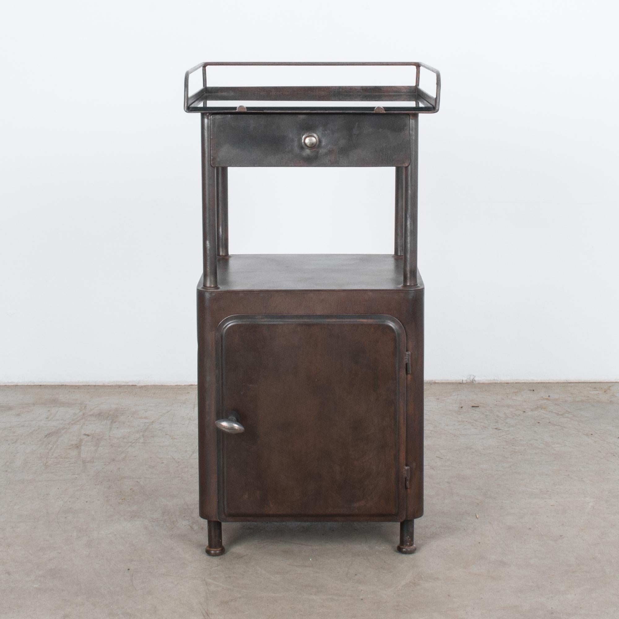 A metal side table from Czechia, circa 1960. Features a drawer, a glass top shelf, a metal lower shelf, and a cabinet. With its geometrical shape and clean lines, this side table is a prime piece of Mid-Century Modern. Clean welding make this piece