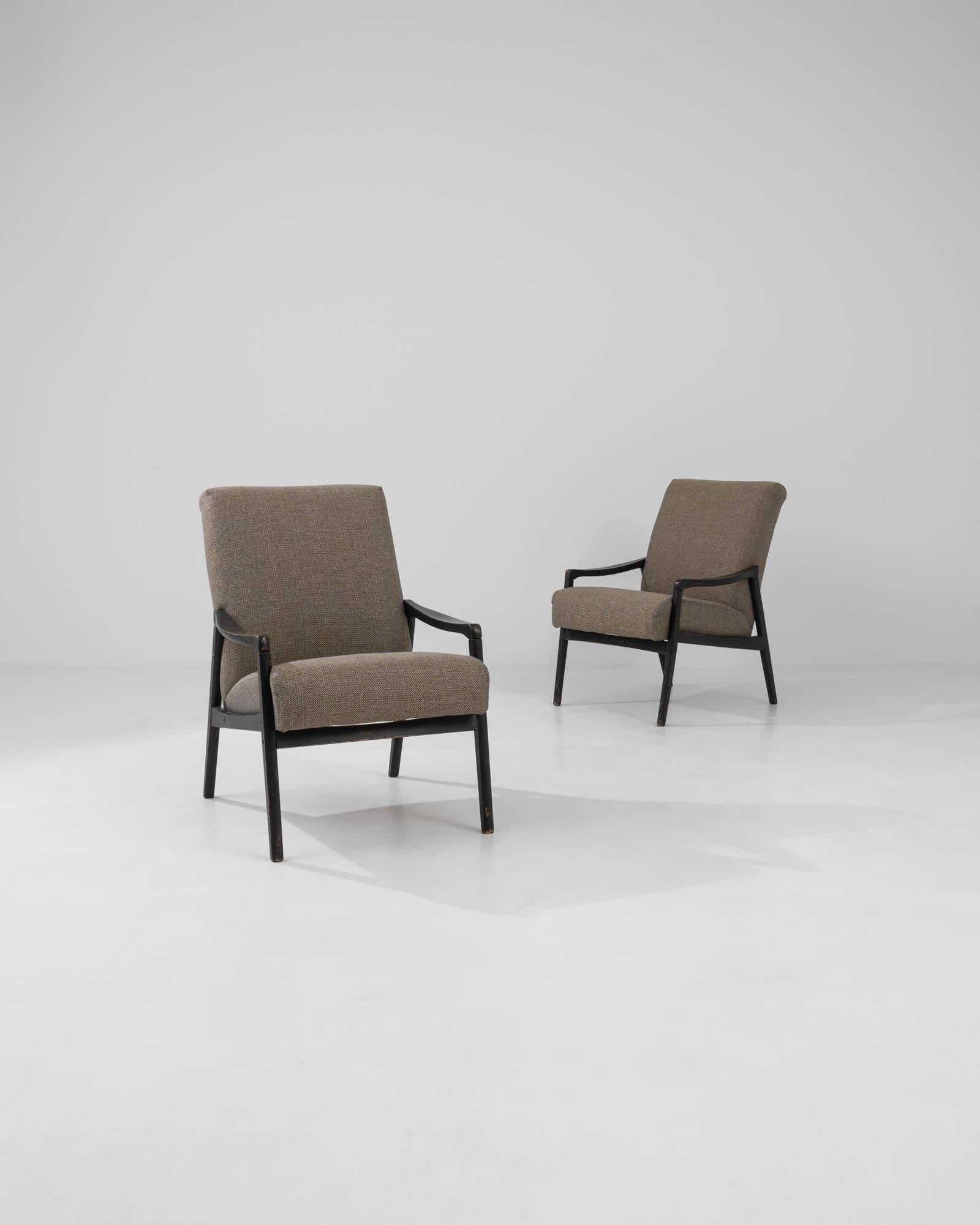 Questa coppia di poltrone imbottite ceche degli anni '60 incarna la sobria eleganza e il design funzionale dei mobili europei della metà del secolo. Caratterizzate da telai puliti e angolari realizzati in legno tinto scuro, le sedie bilanciano la
