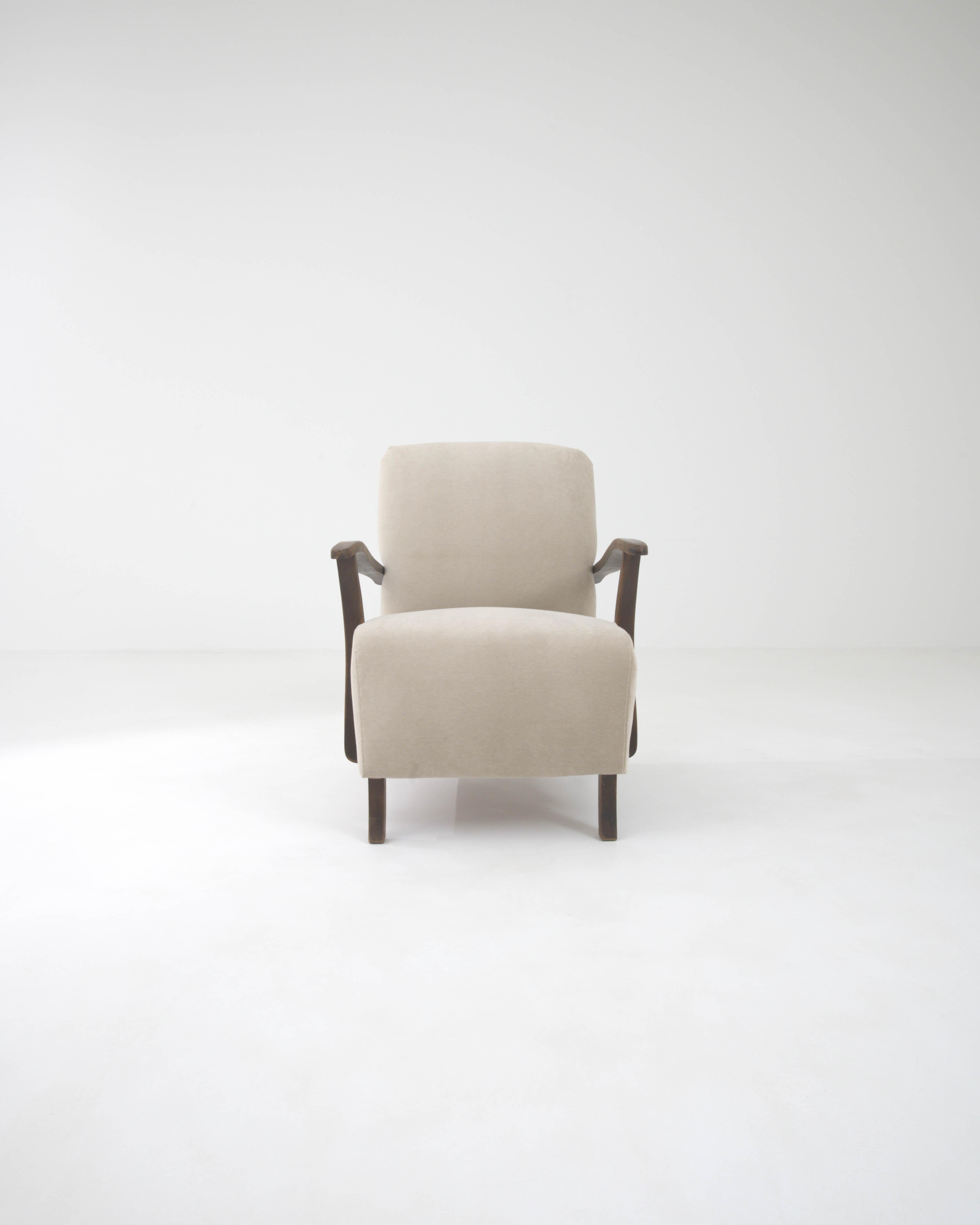 This mid-century modern armchair, crafted in Central Europe, is a medley of contrasts, defined by the stylish curves of the upholstery and the sleek angularity of the armrests and legs. Inclined armrests have a formal effect, giving this armchair a