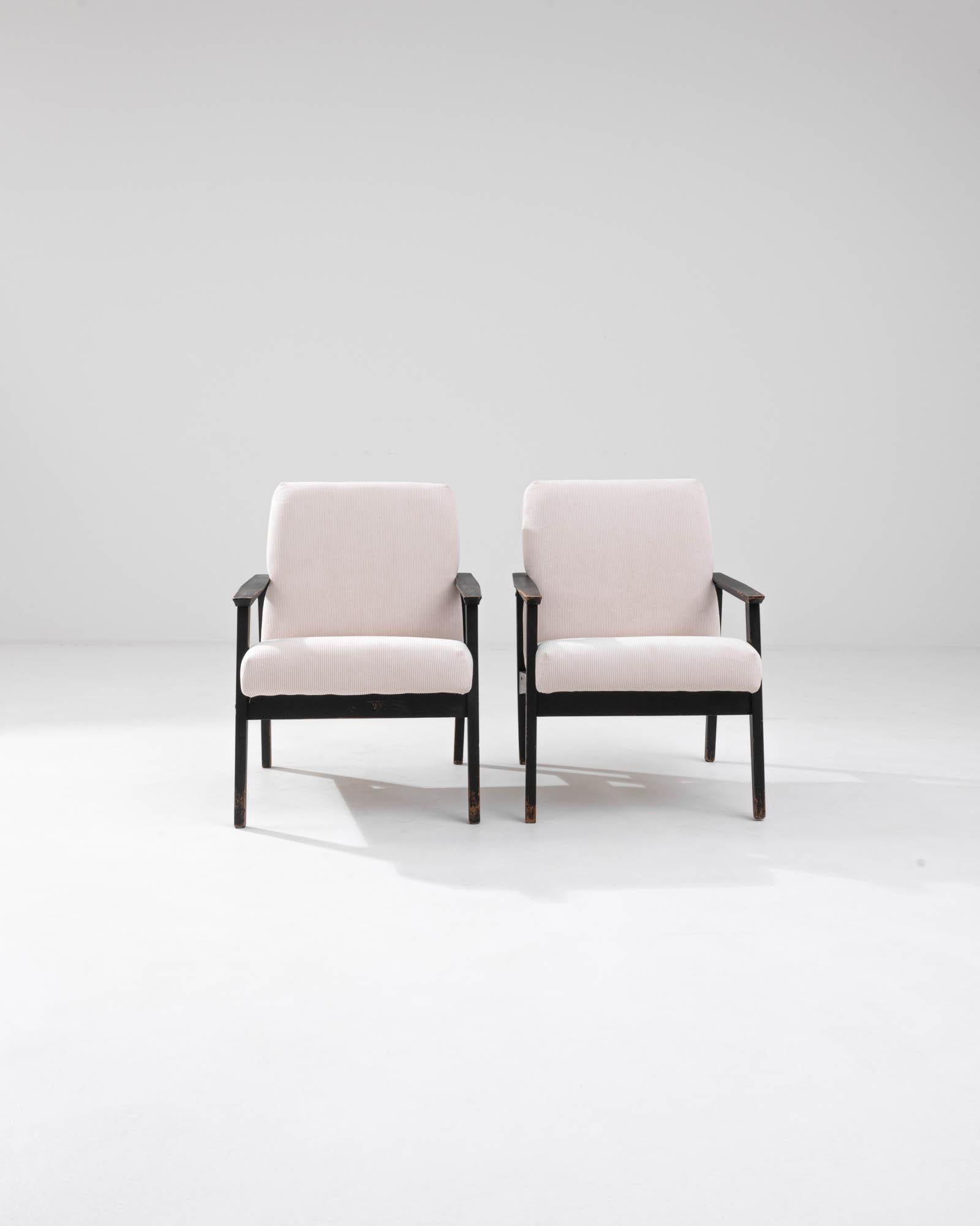 Immerse yourself in the retro allure of our 1960s Czech Pair of Upholstered Armchairs, a duo that beautifully embodies the spirit of mid-century design. These chairs feature a robust frame with sleek black lines that form a striking contrast against