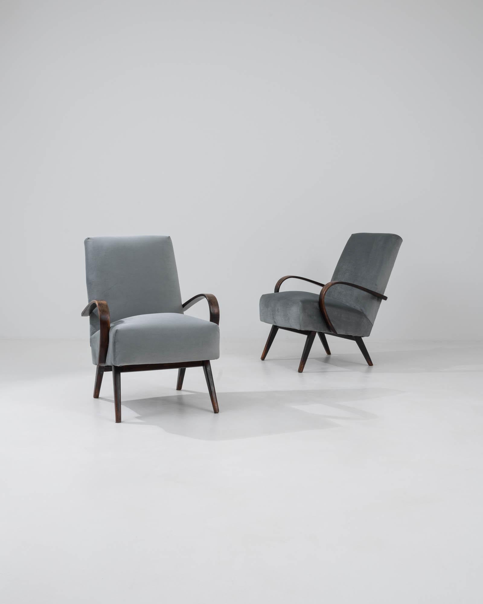 Step into a realm of timeless elegance with this pair of 1960s Czech armchairs by the renowned designer J. Halabala. Exquisitely upholstered in a serene shade of grey, these chairs encapsulate the essence of mid-century modern design with their