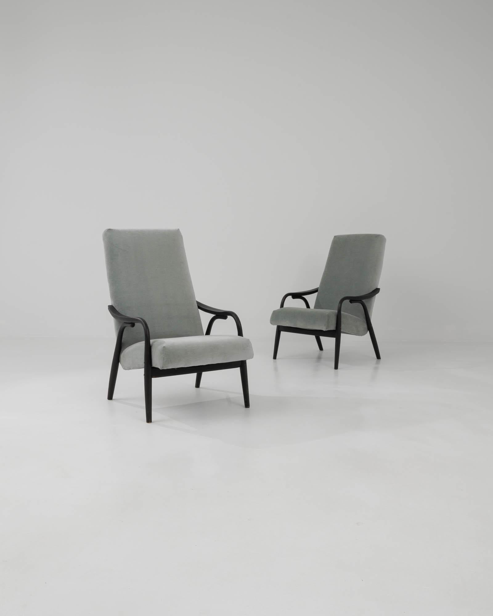 Designed in the 1960s, this pair of Czech mid-century modern armchairs is upholstered in a sophisticated smoky gray soft velvet. They feature sleek, slightly angular wood bases with a black patina, imparting a dynamic quality. The tall rectangular