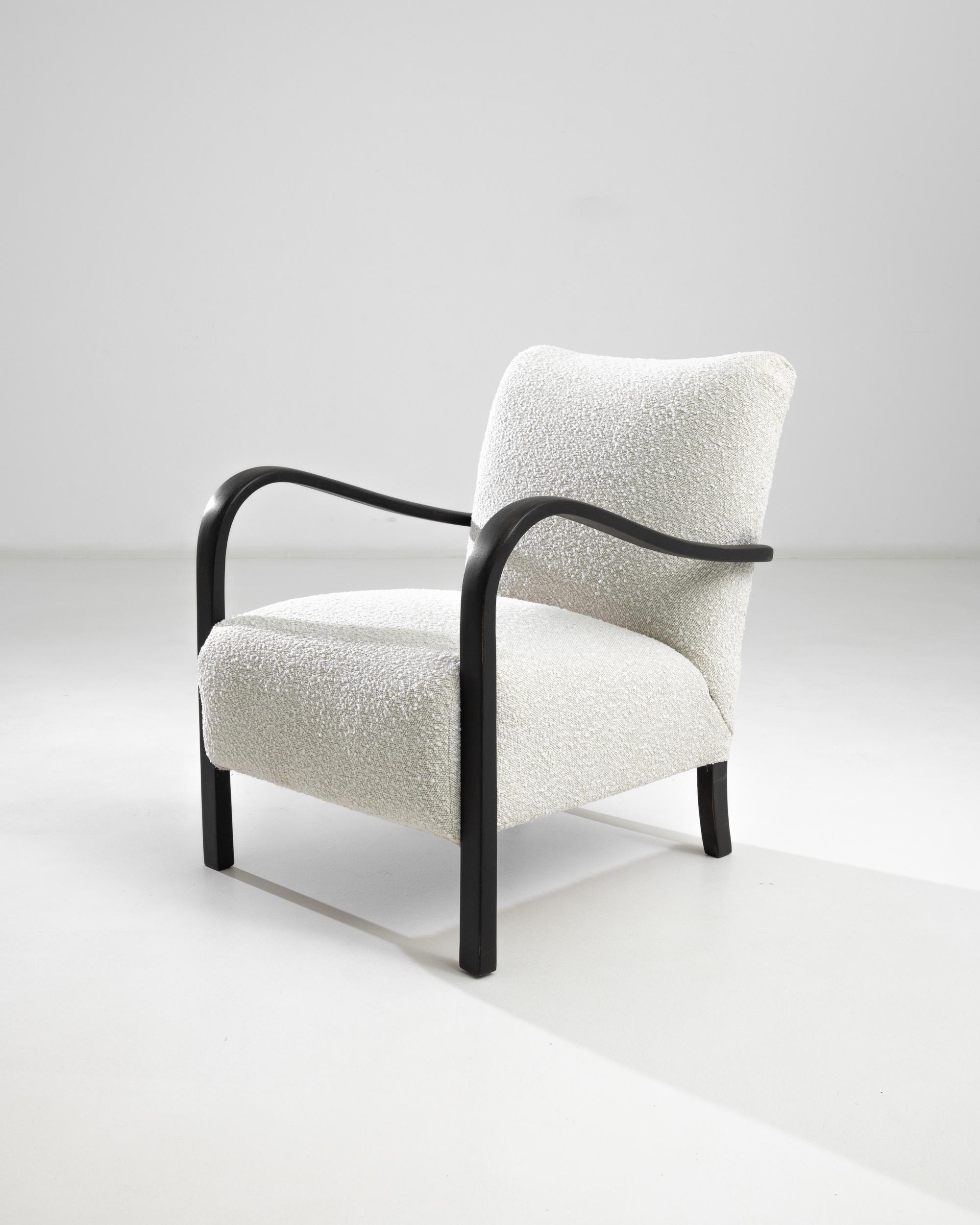 Step into mid-century elegance with the 1960s Czech Wooden Armchair by J. Halabala. This iconic piece boasts sleek black wooden armrests, gracefully curving to provide both style and support. The chair is upholstered in a soft, textured fabric that