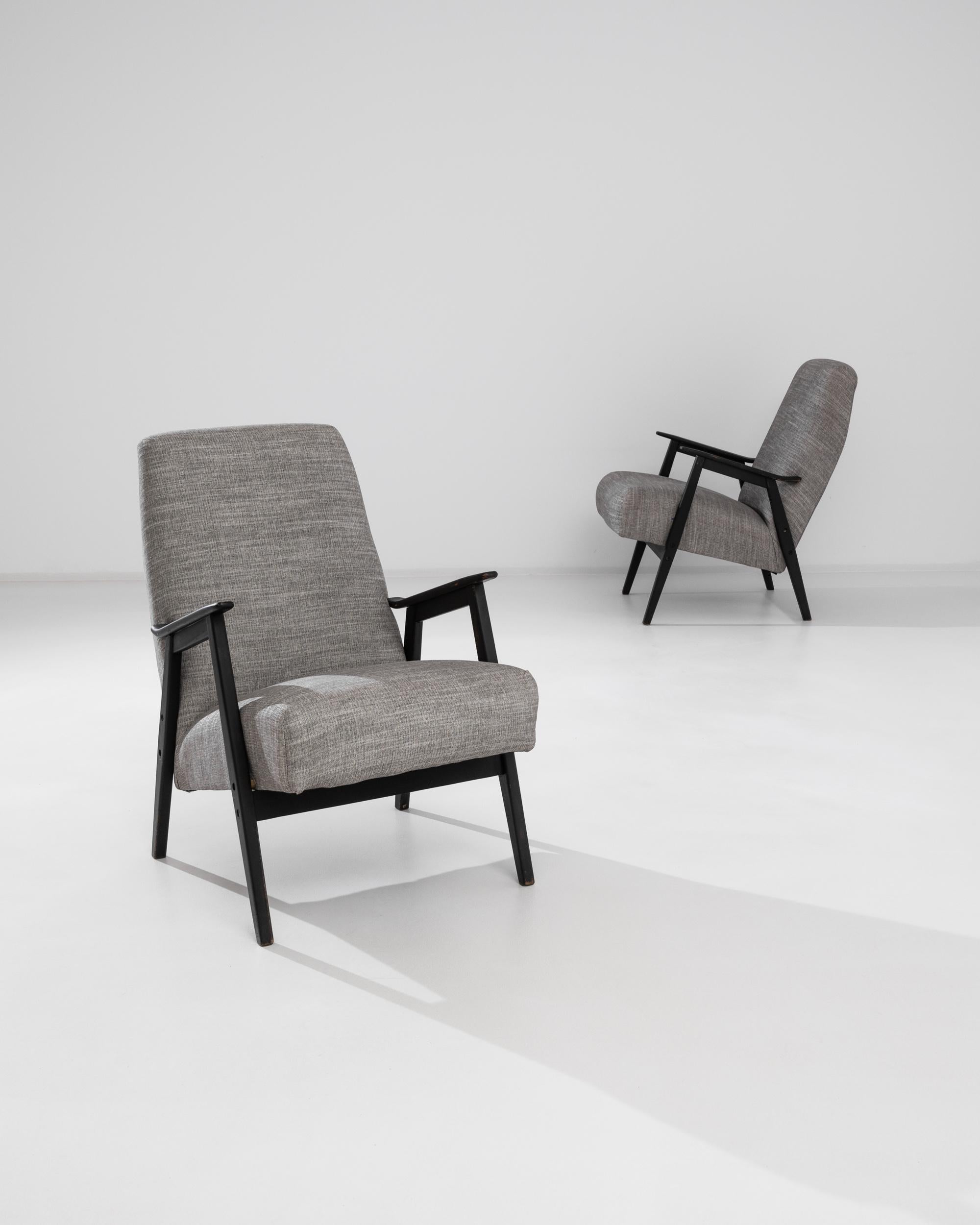 Graphic and stylish, this attractive pair of vintage wooden armchairs cut a striking silhouette. Made in the former Czechoslovakia in the 1960s, the upholstered seat hangs at a comfortable recline between a pair of angular wooden legs. The subtle