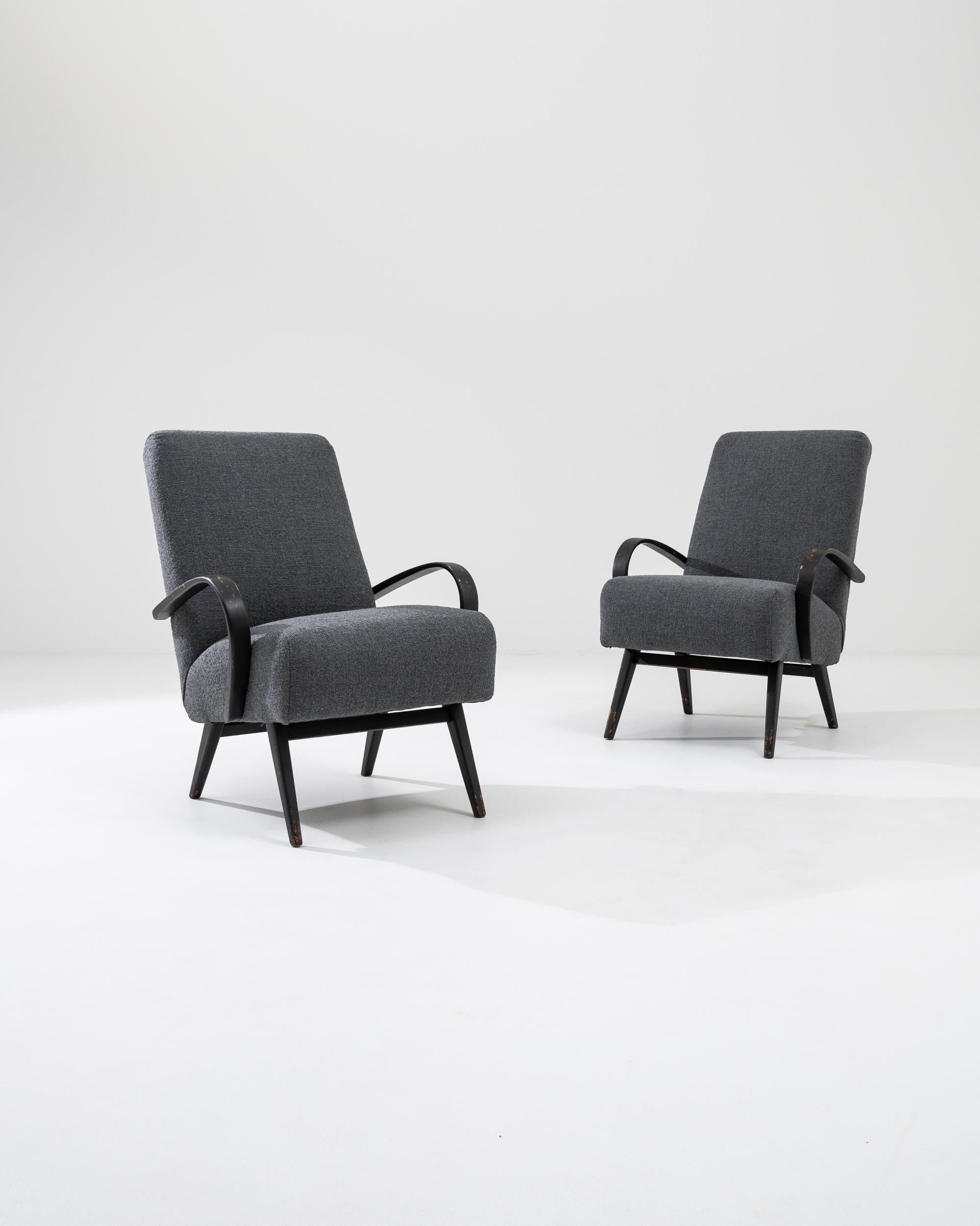 This pair of 1960s Czech wooden armchairs by Jindřich Halabala exemplifies the timeless appeal of mid-century modern design. These chairs feature beautifully curved wooden arms and legs, finished in a rich, dark stain that contrasts elegantly with