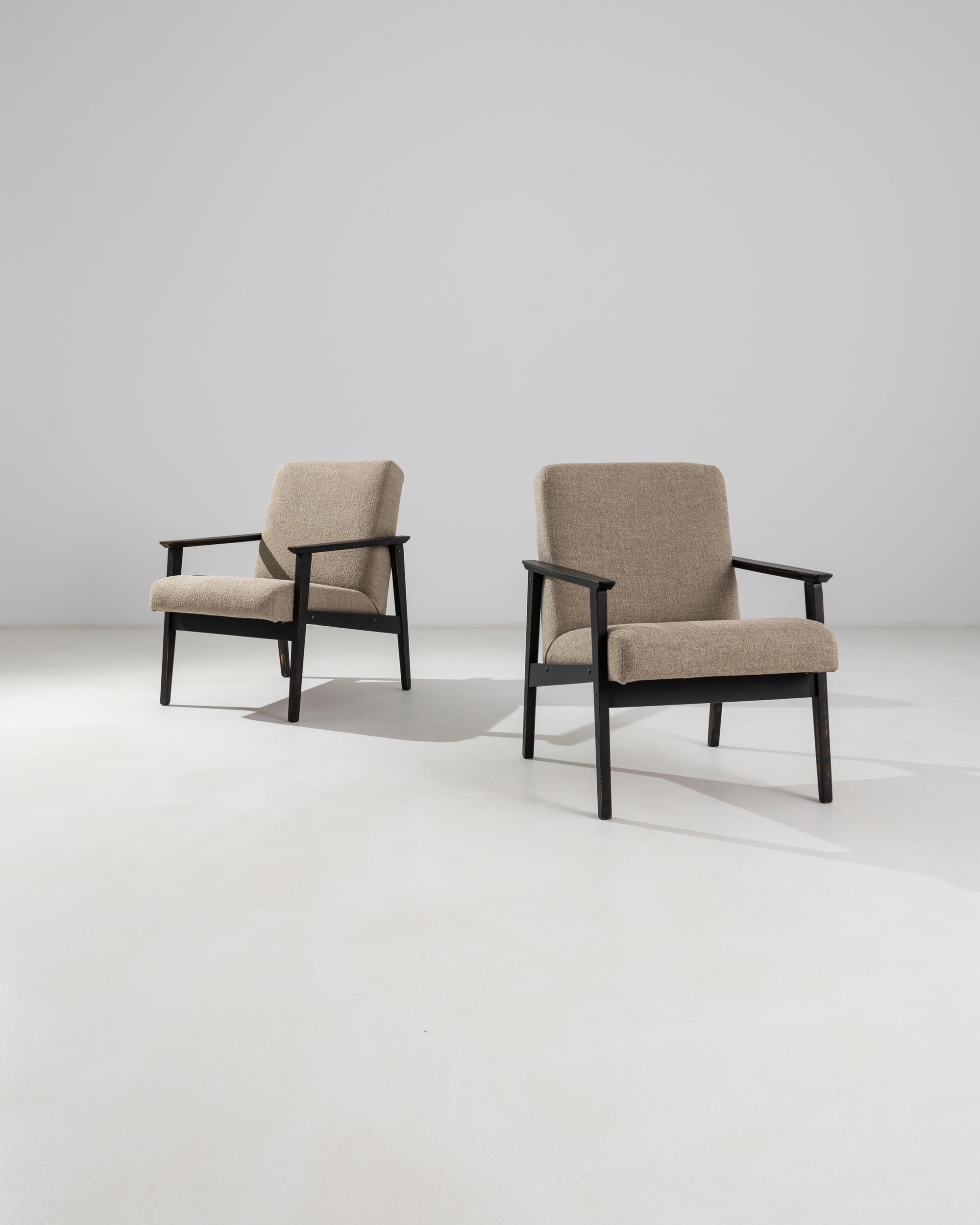 This pair of upholstered armchairs was produced in Czechia, circa 1960. A pair of sedate armchairs upholstered with a soft sand boucle fabric, featuring a slightly reclined back and a large seat for a comfortable posture. Completed by a minimal