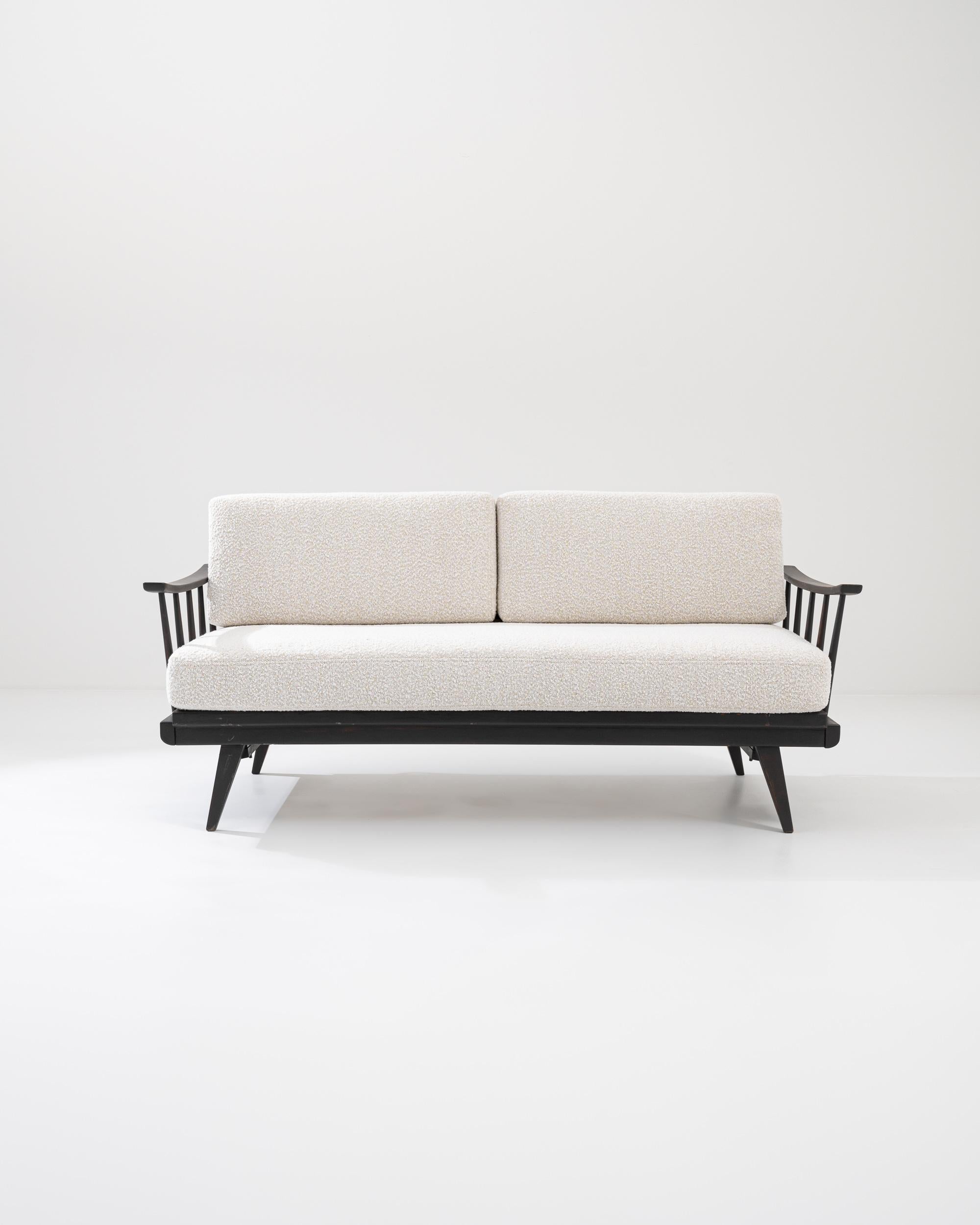 This wooden upholstered sofa was produced in Czechia, circa 1960. An elegant sofa elevated upon splayed tapered feet, refurbished with a soft boucle upholstery in a powder tone. The plump cushions ensure a relaxed posture, while the original wooden