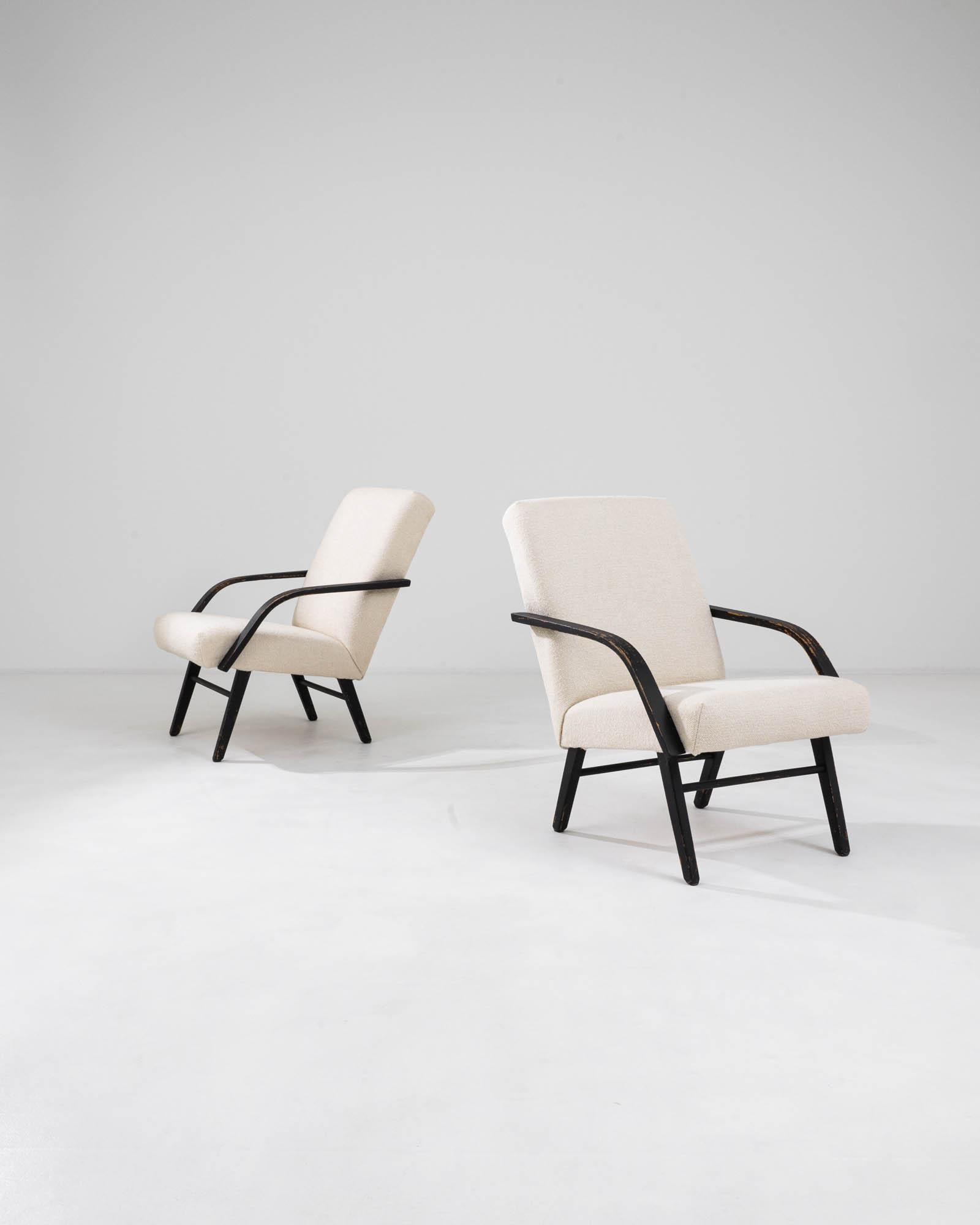 Immerse yourself in the mid-century allure with a set of two 1960s Czechia Upholstered Chairs. Upholstered in a timeless white hue, these chairs exude elegance, while the sleek black arms and legs provide a striking contrast. Crafted with meticulous