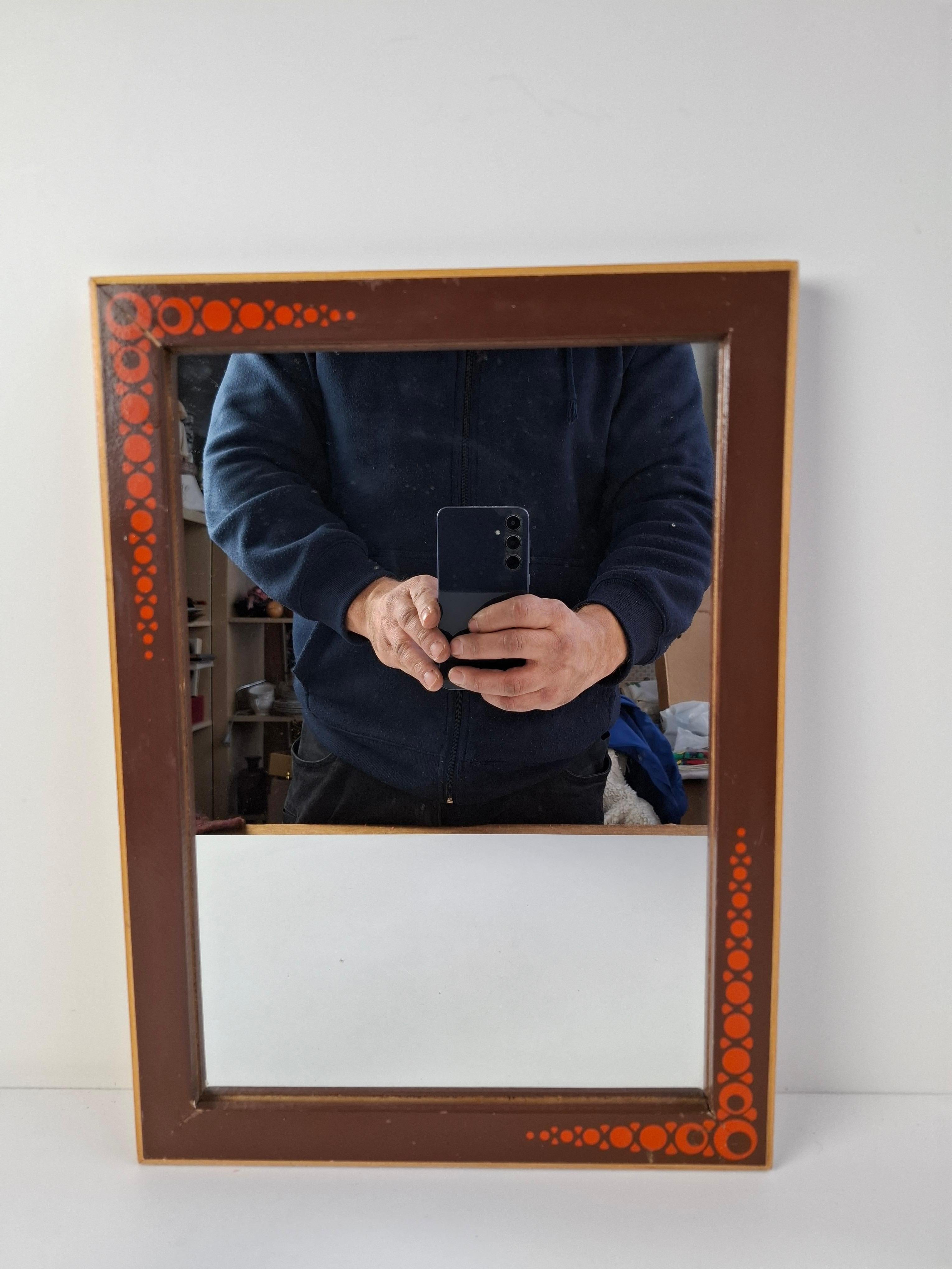 Miroir mural du milieu du siècle produit dans la Tchécoslovaquie des années 1960, doté d'un cadre en bois orné de détails graphiques circulaires rouges stylisés. Le miroir affiche une patine de vieillissement authentique, ajoutant de la profondeur