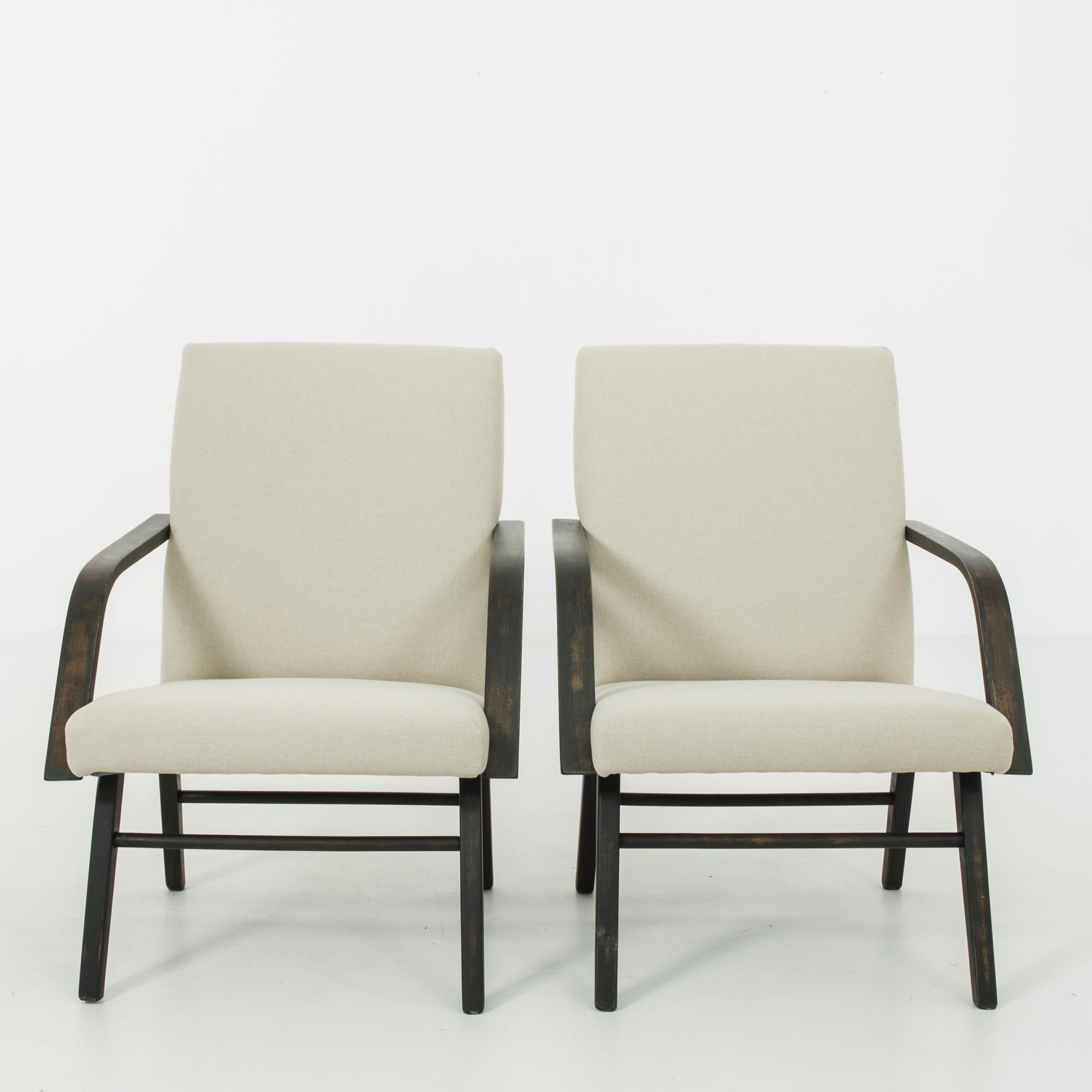 This pair of upholstered wooden armchairs was made in Czechoslovakia, circa 1960. Distinctive angular armrests and tapered, splayed legs give the chairs a contemplative silhouette, underscored by geometric seat cushions. The newly upholstered seats
