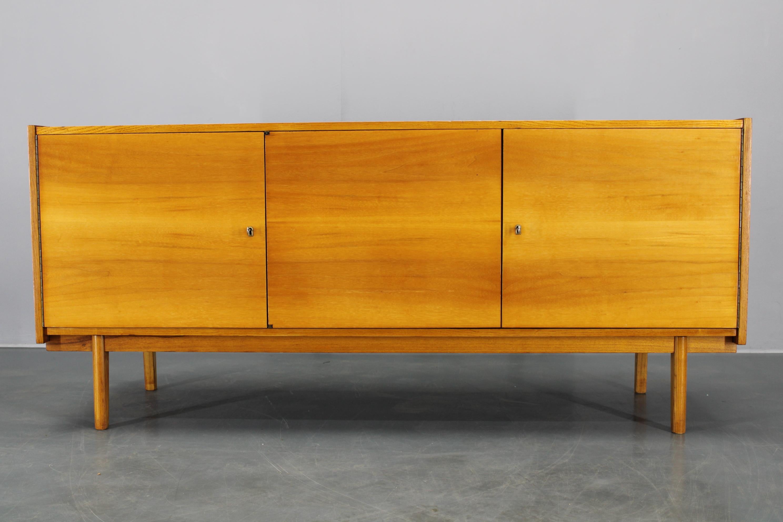 Vintage sideboard made in Czechoslovakia circa 1960s, featuring maple veneer and solid maple wood construction. This sleek, minimalist piece offers three lockable doors and stands on sturdy round legs. The front is elegantly finished in a high
