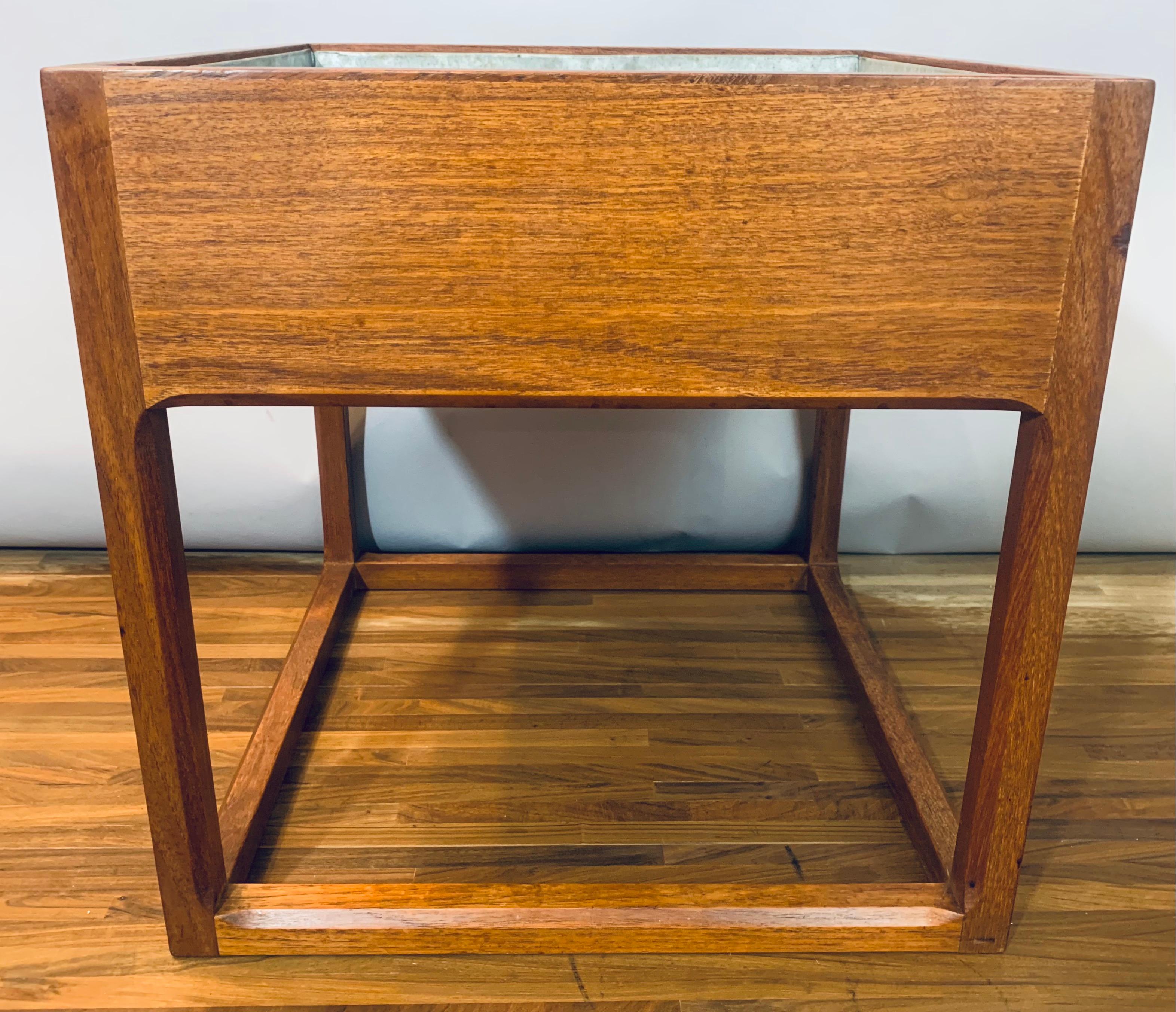 1960s Teak cubic planter with feature chamfered legs and supports. The removable metal liner is easily removed with two handles at either side. I have checked and It's watertight and is in good condition considering its age and use. The planter is