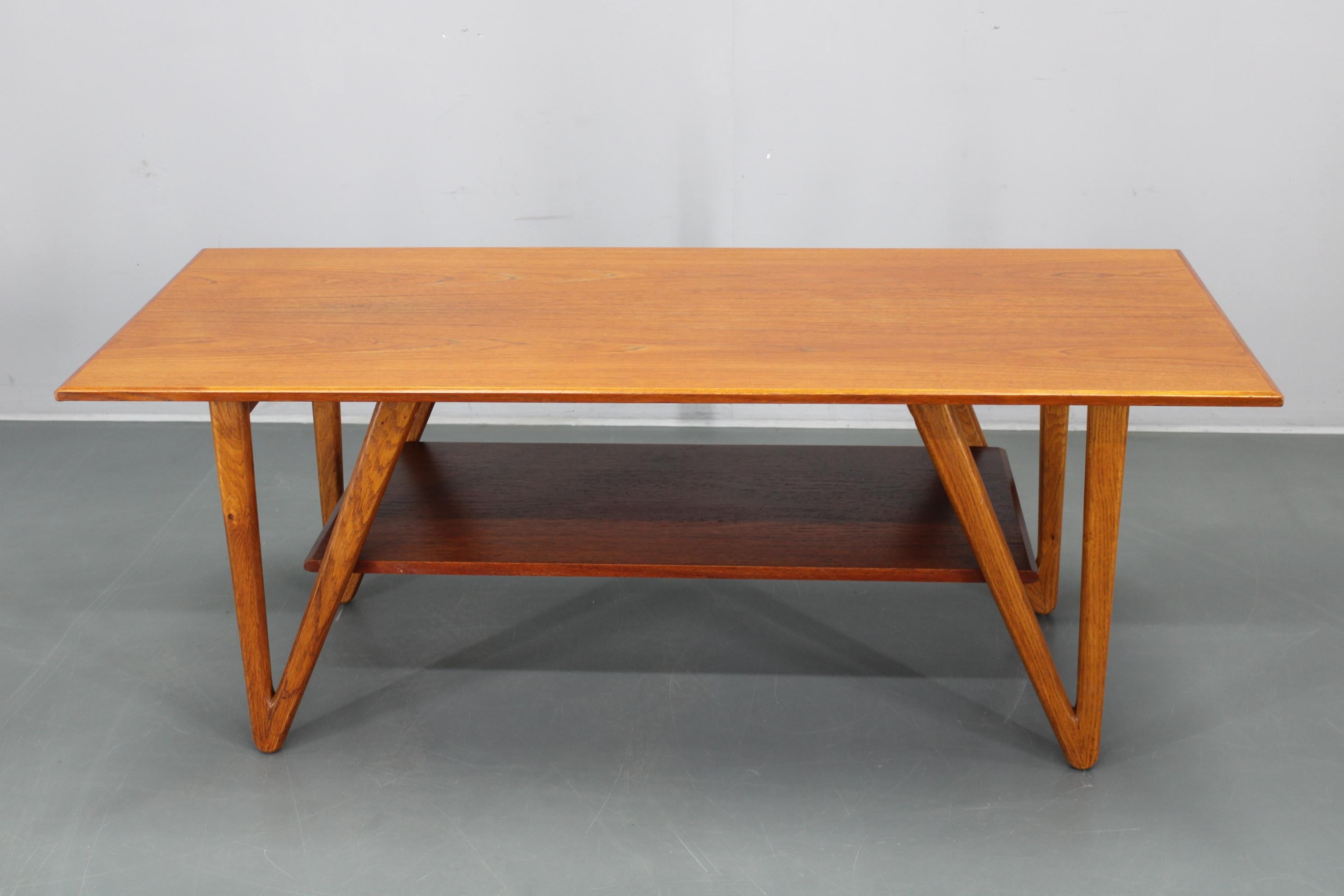 This exceptional 1960s Danish coffee table combines a teak-veneered top with a solid oak base featuring sharply angled sculptural legs. Designed and produced in Denmark, it expresses the refined simplicity and functional elegance central to