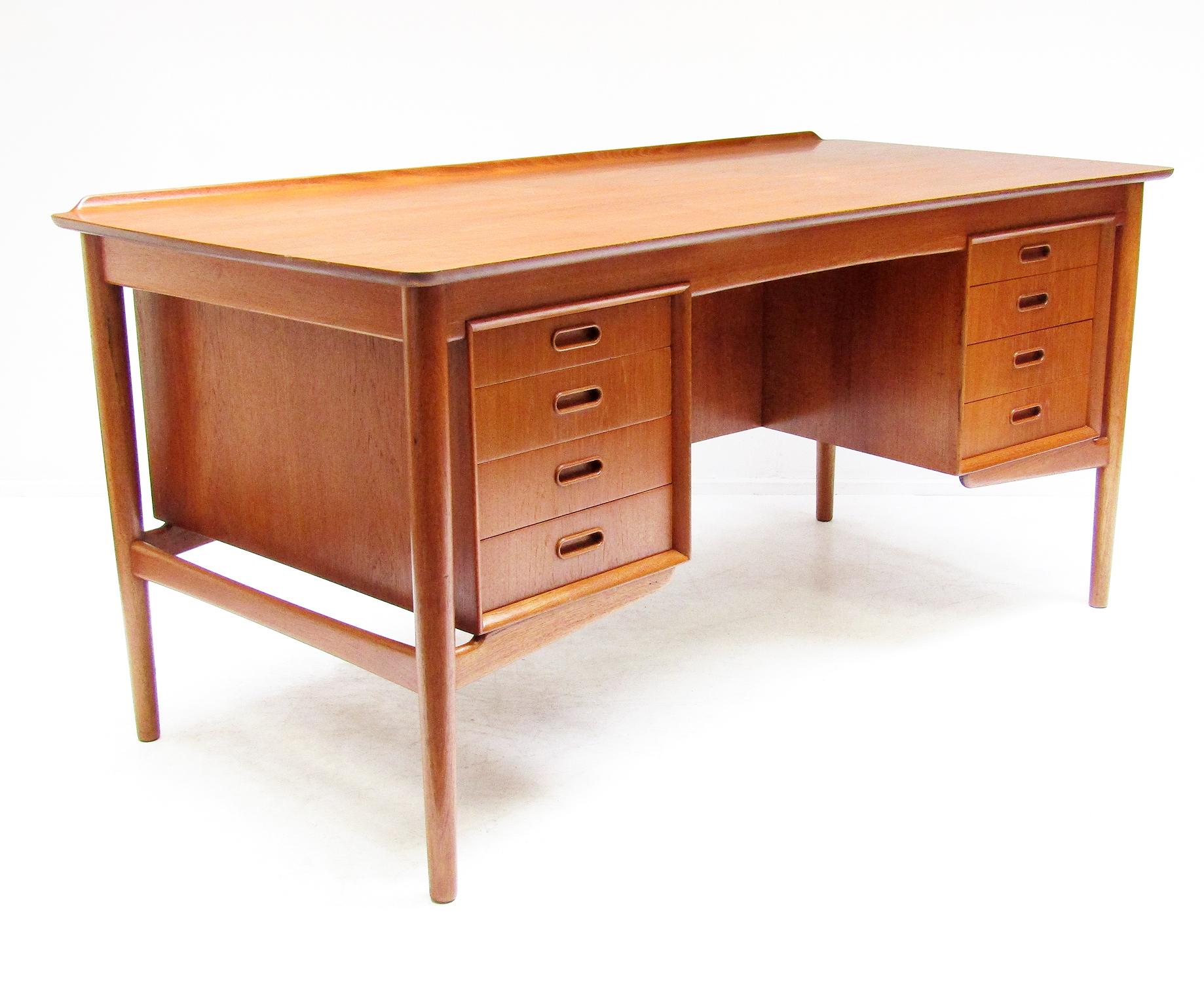 A 1960s desk in teak by Danish designer Svend Aage Madsen for Sigurd Hansen.

This finely crafted desk has a subtly curved writing surface with sculpted rear lip. It sits on tapering legs, with a bank of four smooth drawers on each side of the