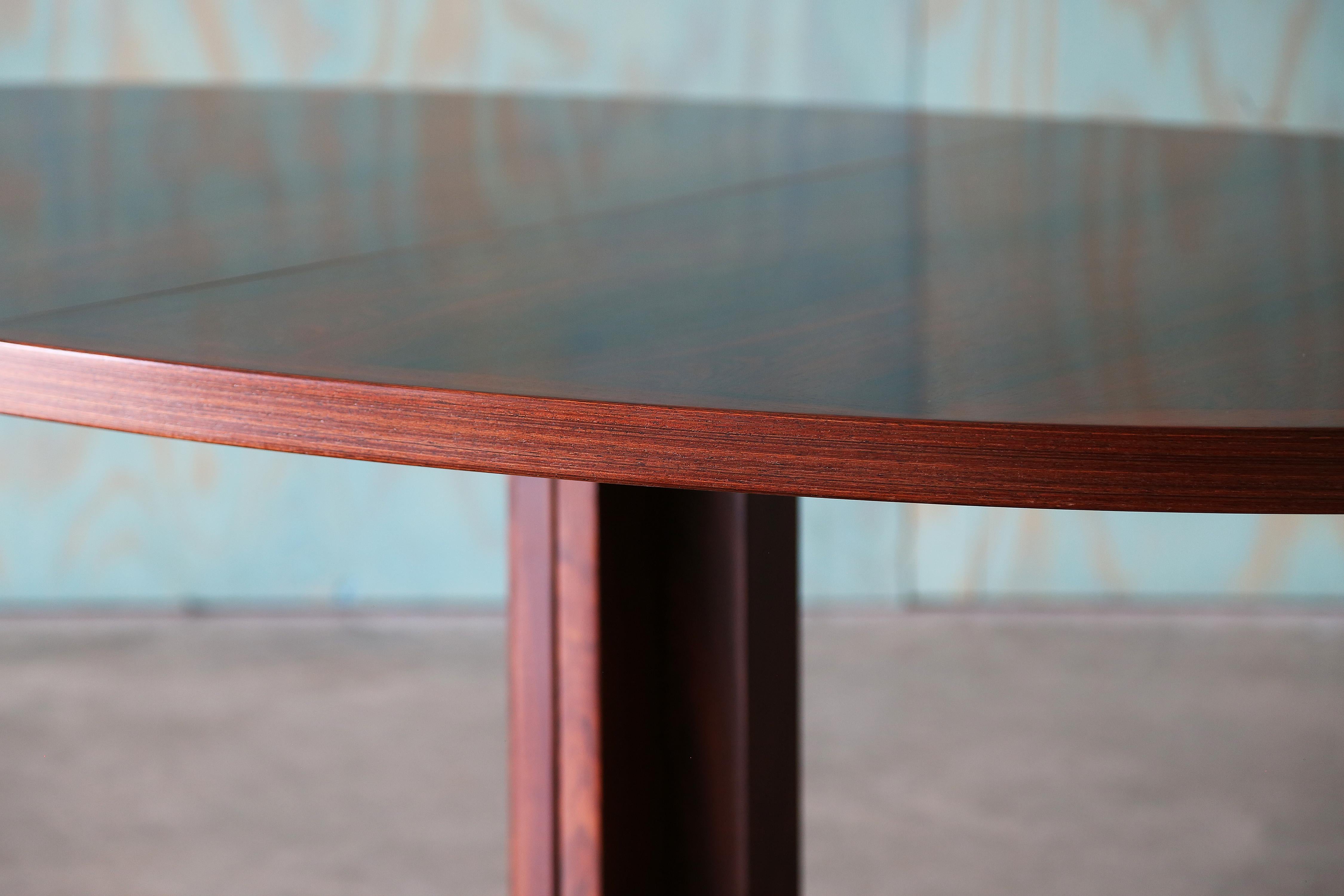 Expressive rosewood veneer top on this Extendable dining table designed by John Mortenson for Heltborg Møbler.  Solid rosewood base forms a pedestal when together and when extended with one or two leaves the pedestal pulls apart with a unique T