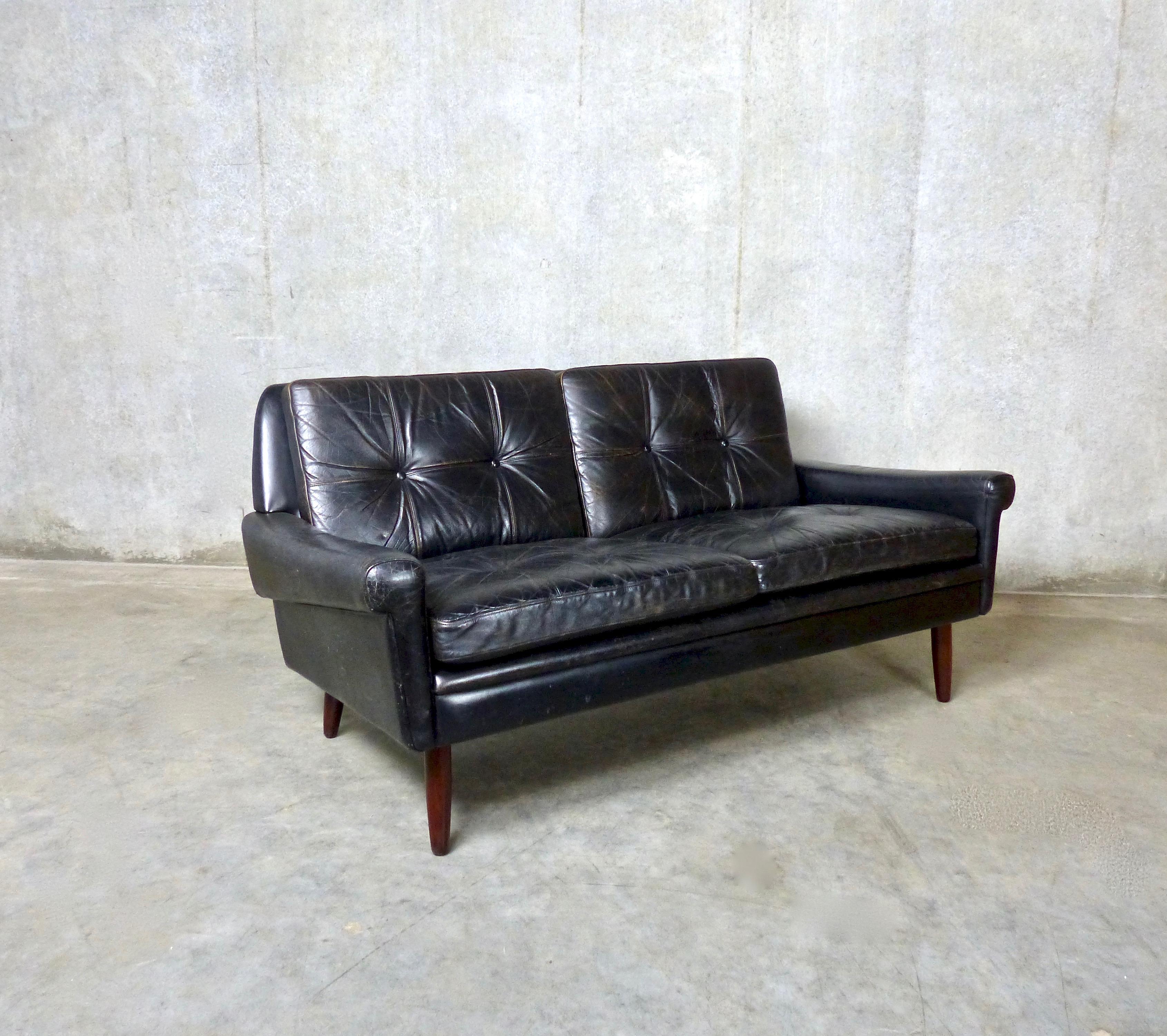 A tufted, black leather, two-seat sofa designed by Svend Skipper in the 1960s and made by Skipper Mobler in Denmark. This compact but luxurious sofa, in original leather, sits on rosewood tapered legs. A Classic Mid-Century Modern