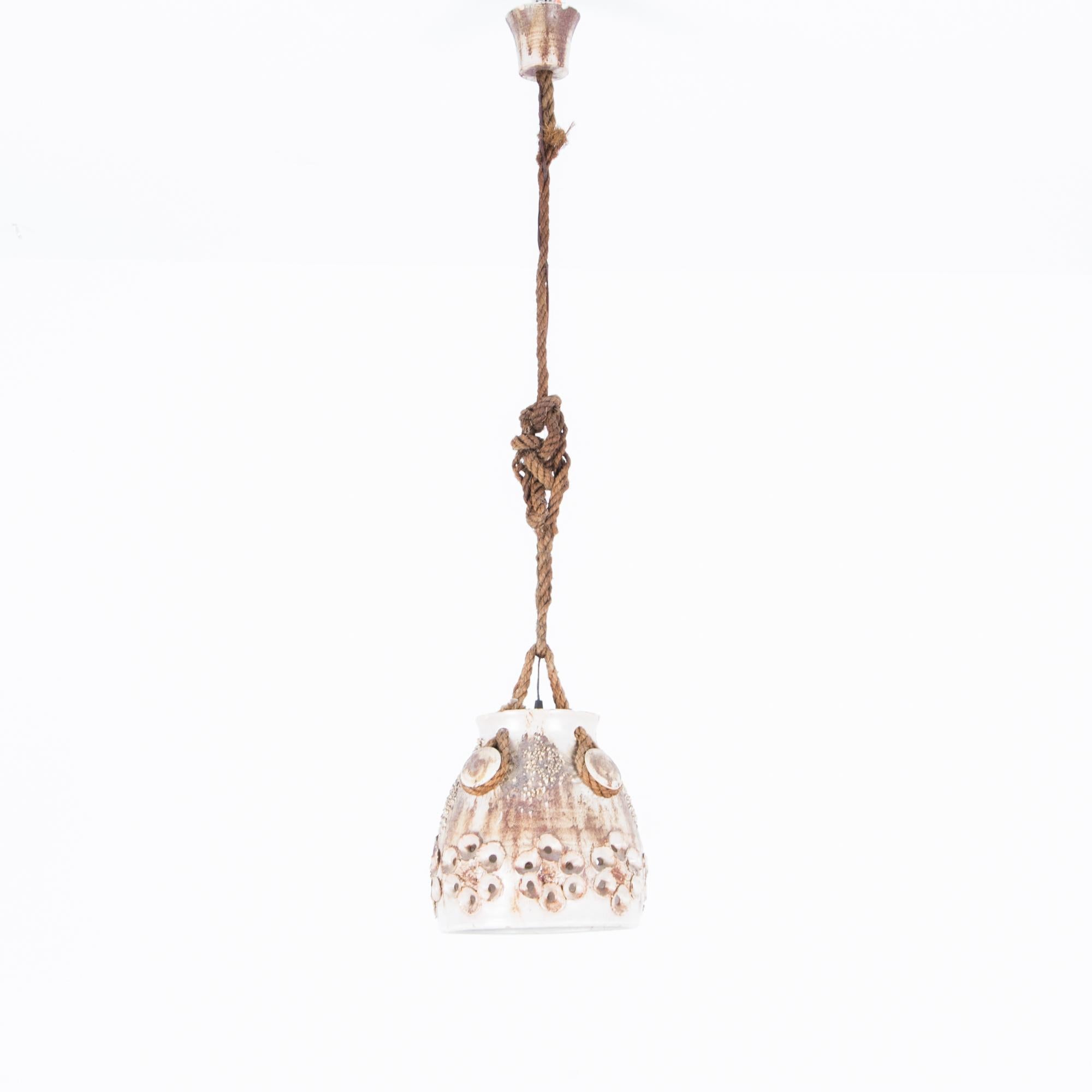 Made in Denmark in the 1960s, this ceramic pendant light has great organic texture. A glazed ceramic light fixture featuring a rustic floral pattern is sustained by a knotted rope, attached to ceramic cleats for a nautical effect. The shell-like
