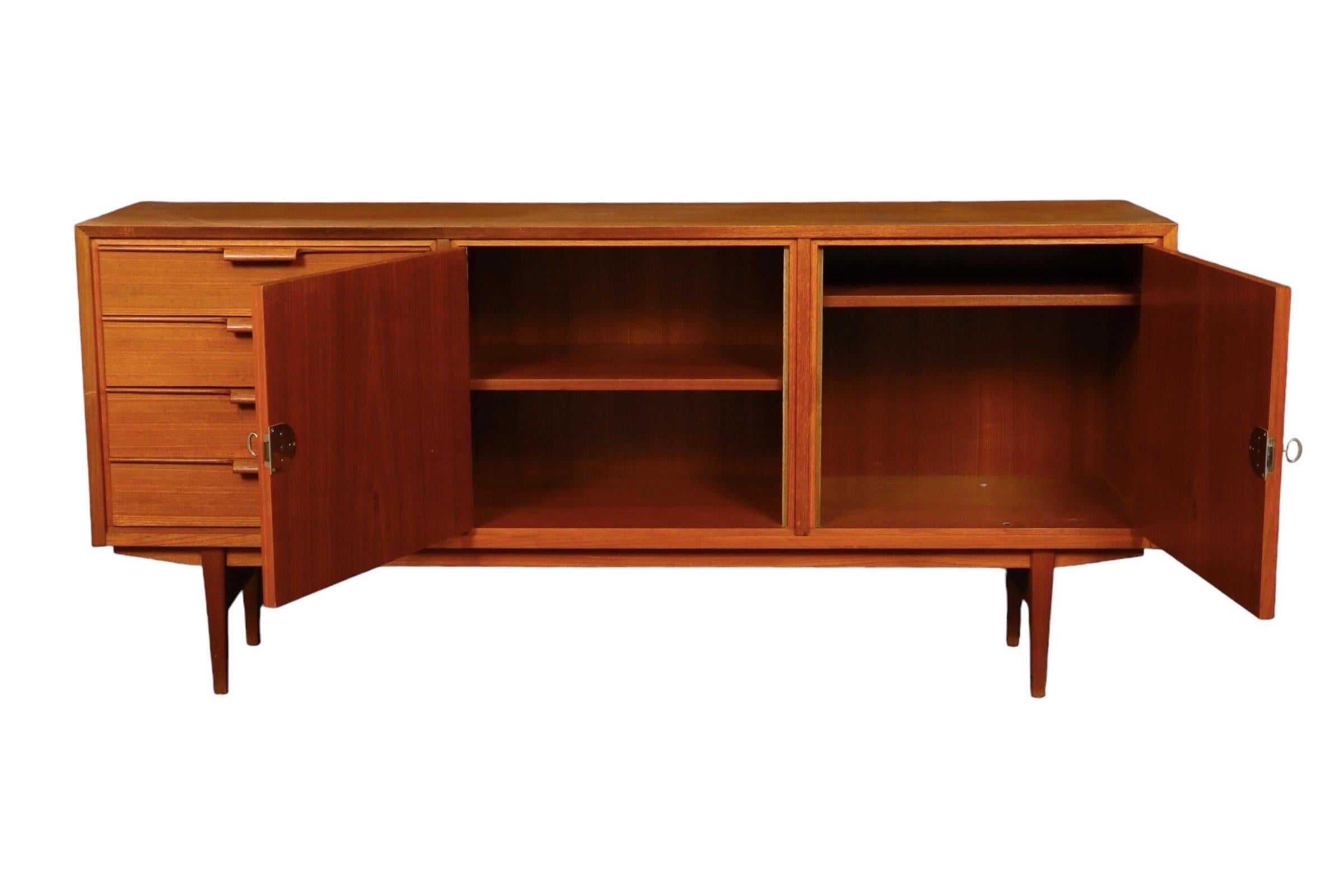 1960’s Danish Mid-Century Modern sideboard made of teak. Four drawers on the left open with curved bar handles. The locking cabinet to the center right houses a single shelf. Tapered legs are supported with a thick stretcher at each end.
 