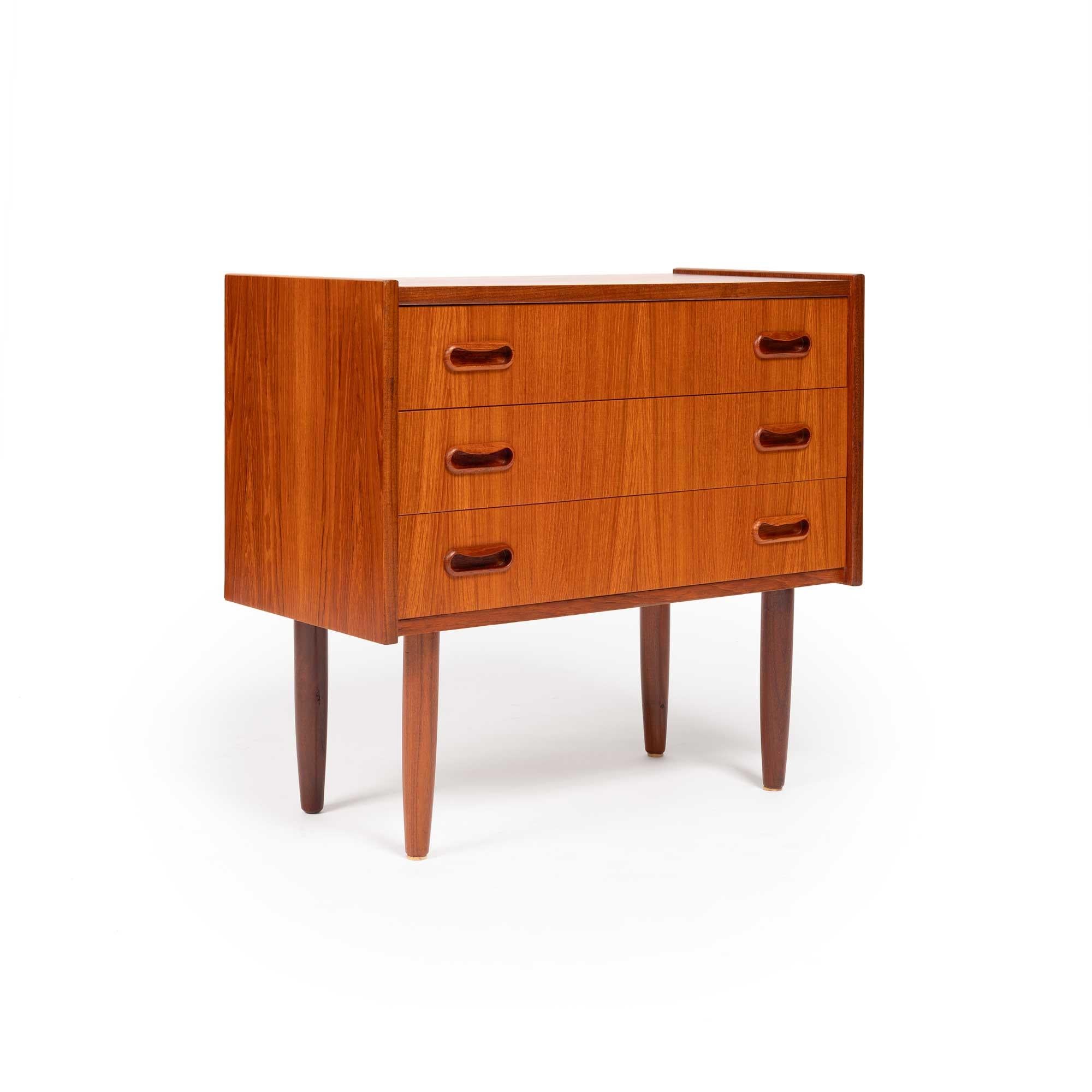 A stunning vintage Danish teak chest showcasing a rich, beautiful teak grain. Its compact size makes it an ideal choice as an accent piece, entryway table, or nightstand. Featuring three drawers with elegantly sculpted pulls, this piece embodies the